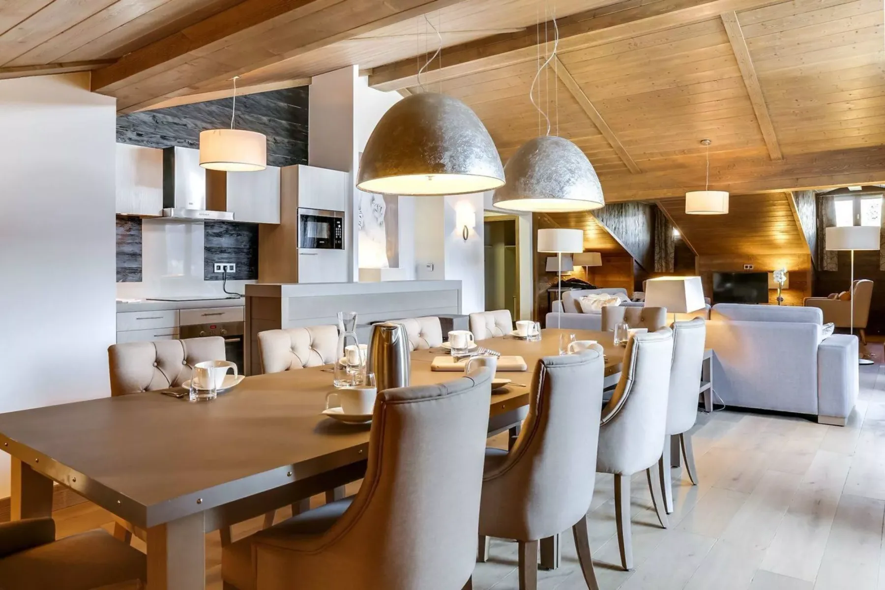 An open-plan dining and living area with a long table beneath a sloped wooden ceiling.