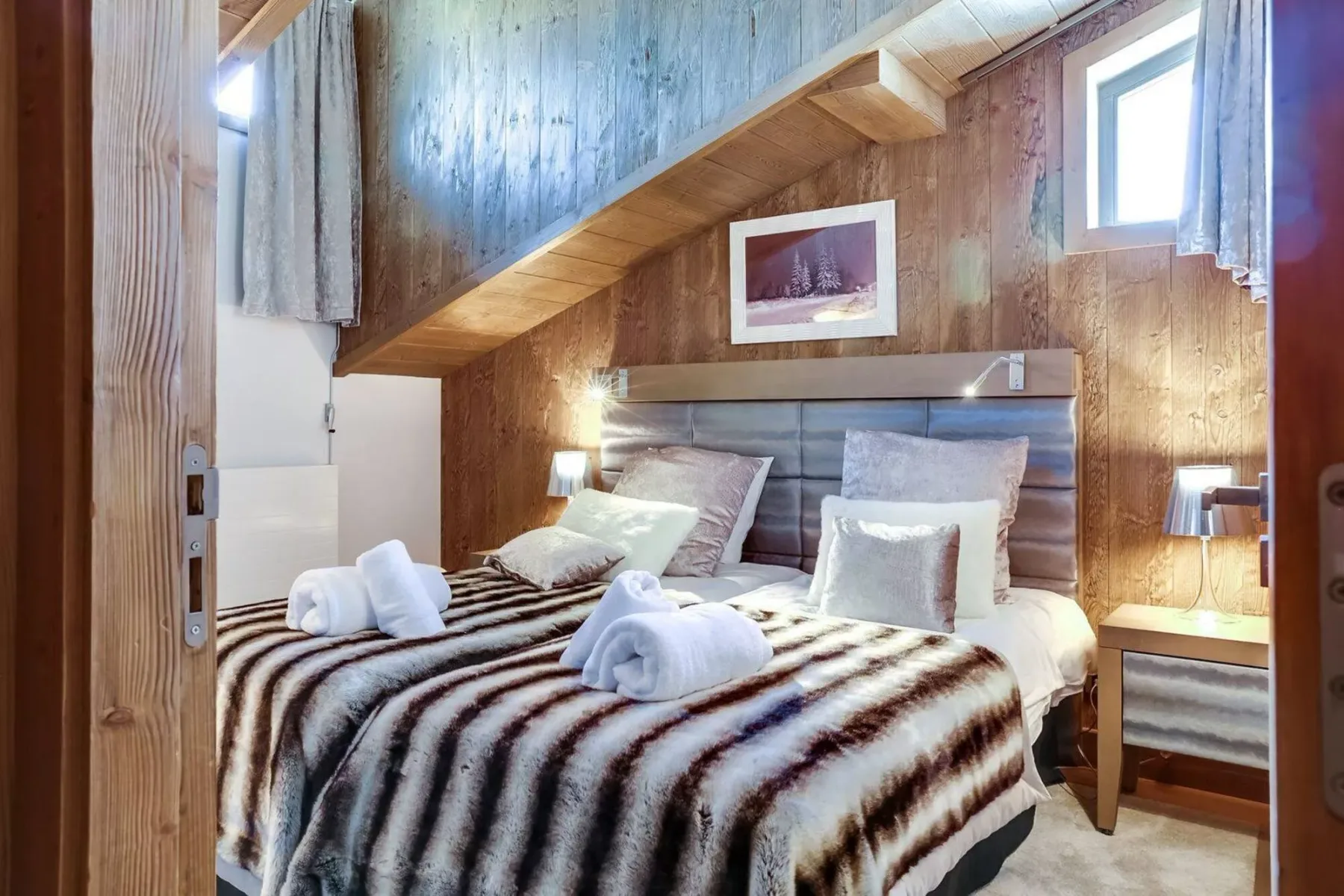 A bedroom with a neatly made bed beneath a wooden staircase.