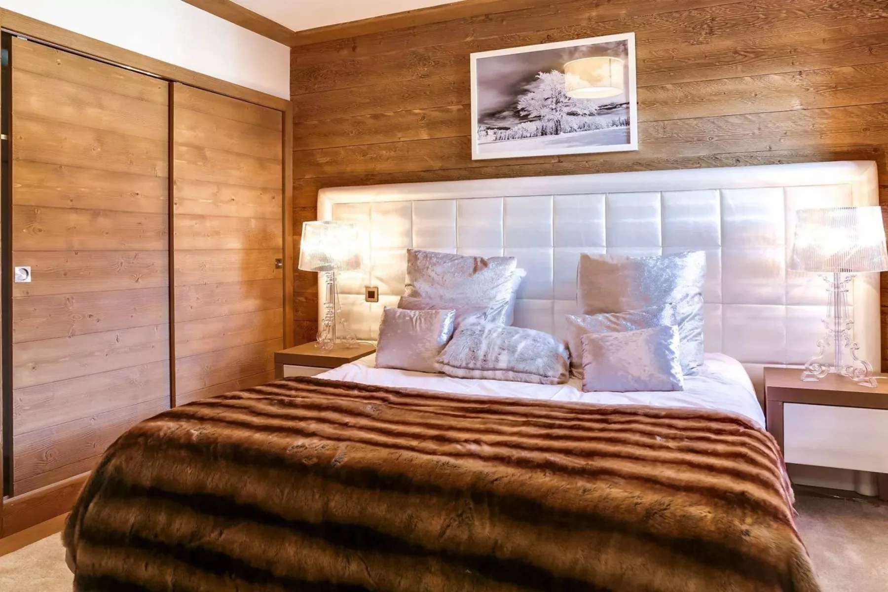 A bedroom with a bed against wood-paneled walls and matching bedside lamps.