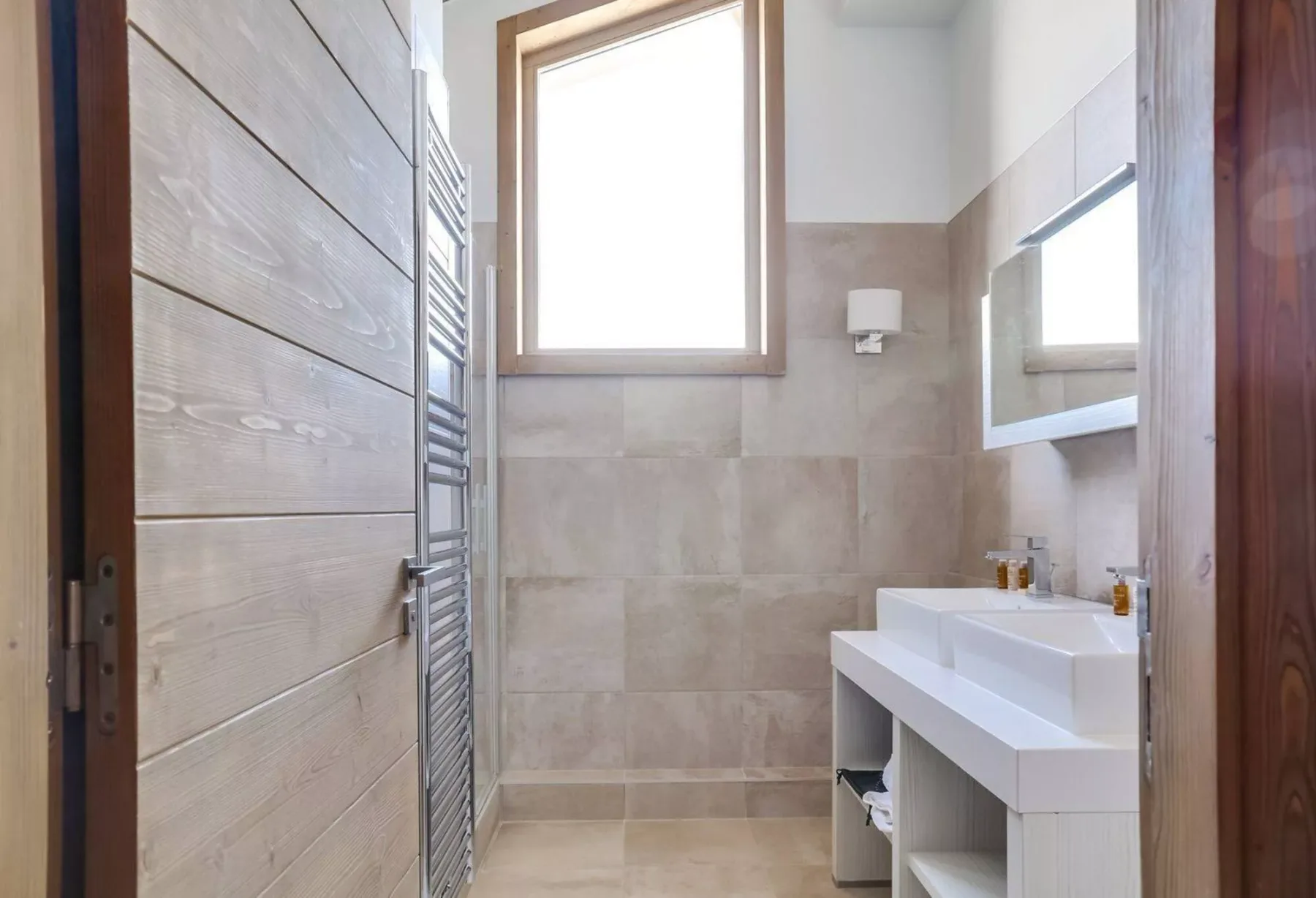 A bright bathroom with a tiled wall, a window, and a sink.