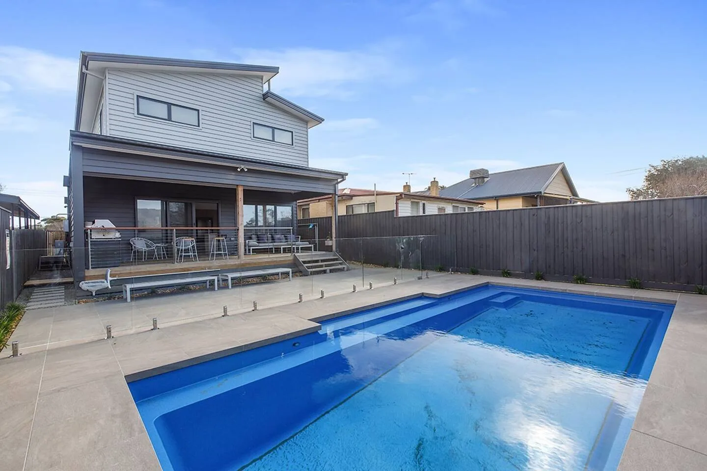 Una piscina al aire libre ocupa el patio junto a una casa y una terraza.