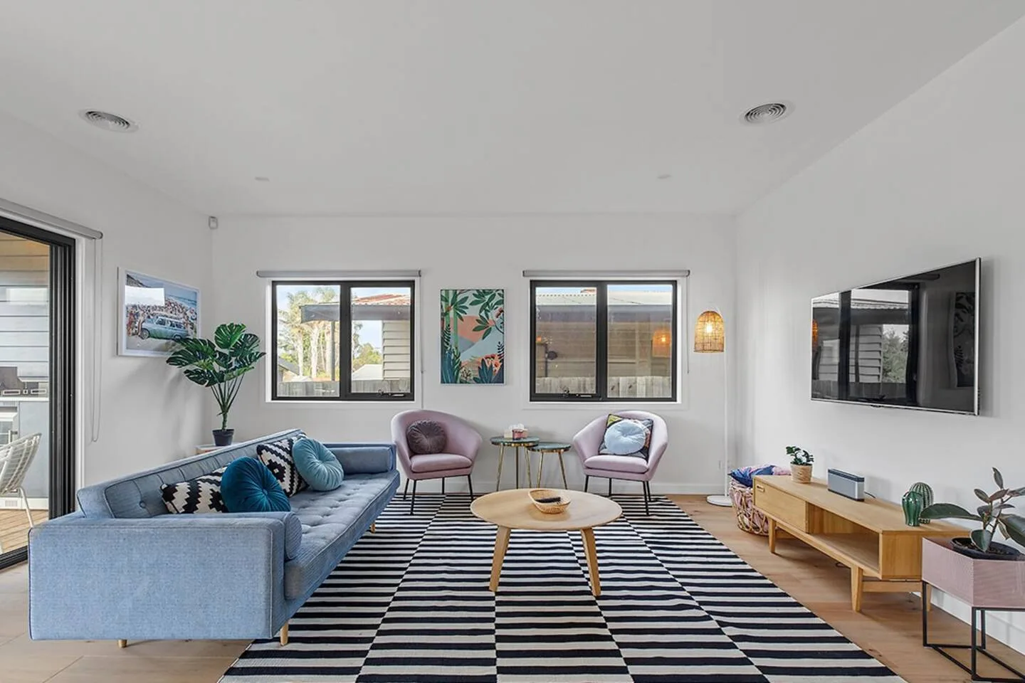 A bright living room has seating arranged around a coffee table on a striped rug.