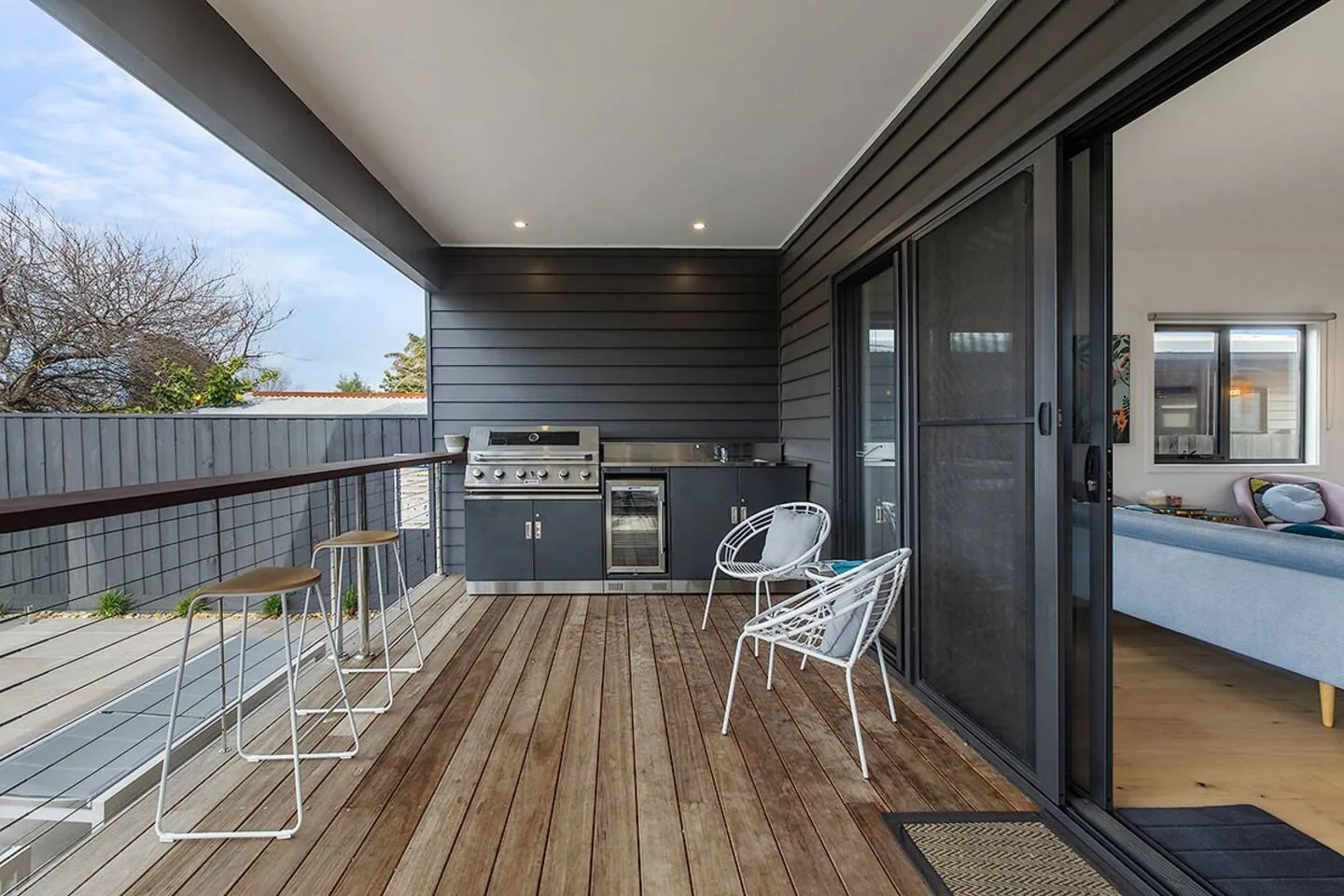 A covered patio has an outdoor kitchen, bar seating, and two chairs.