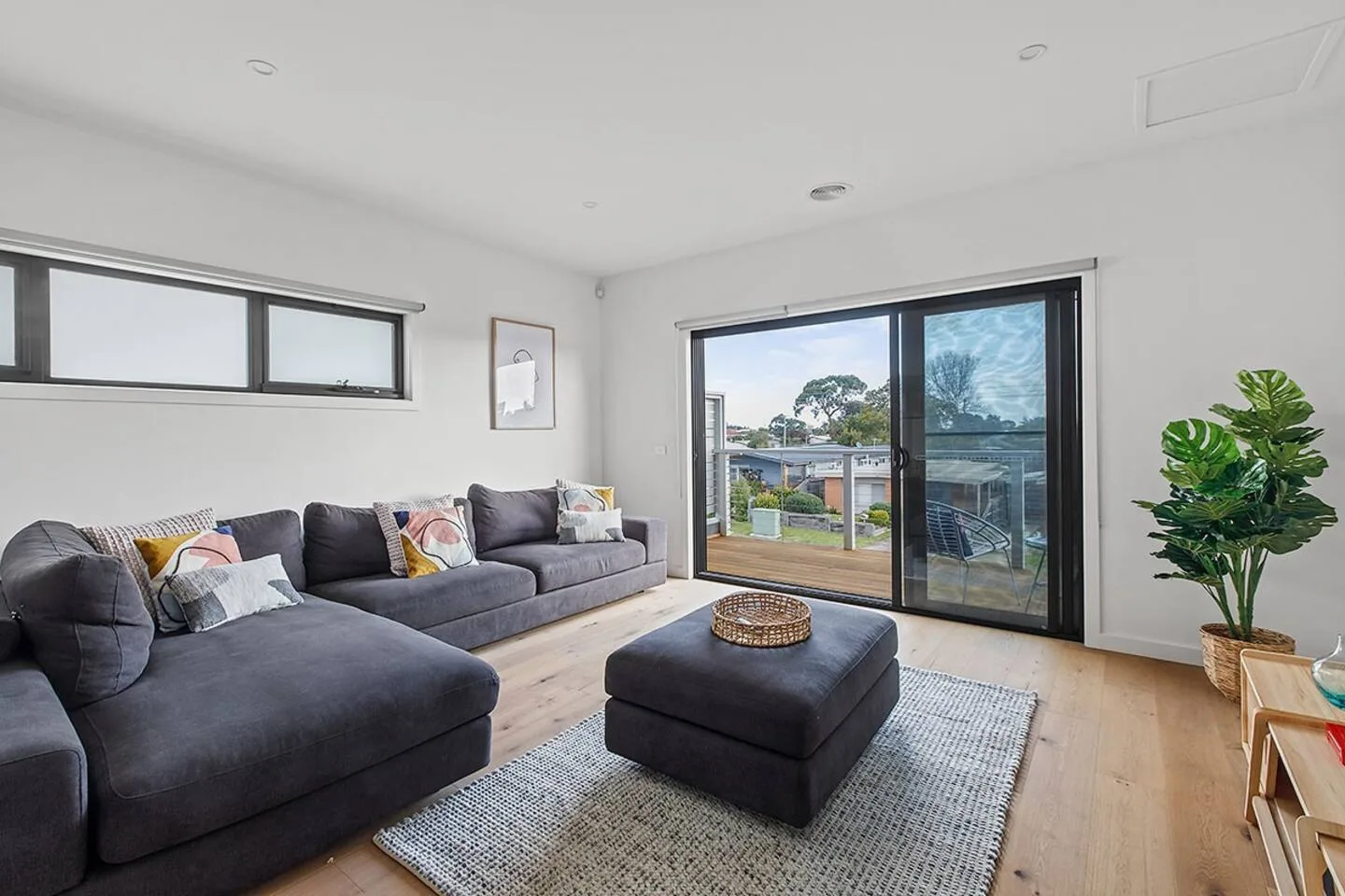 A bright living room with a sectional sofa, ottoman, and sliding glass doors.