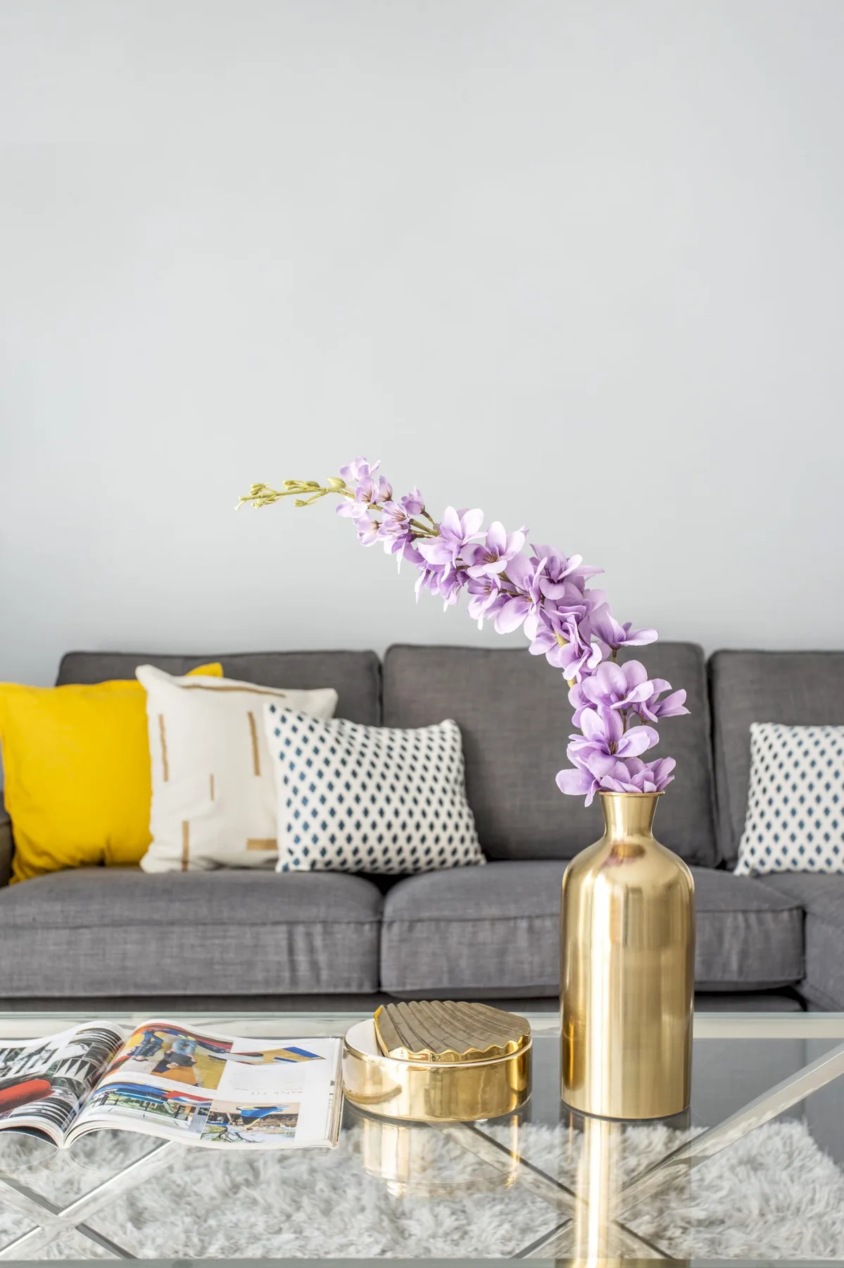 Sala de estar con asientos grises, cojines de colores y una mesa de centro de vidrio.
