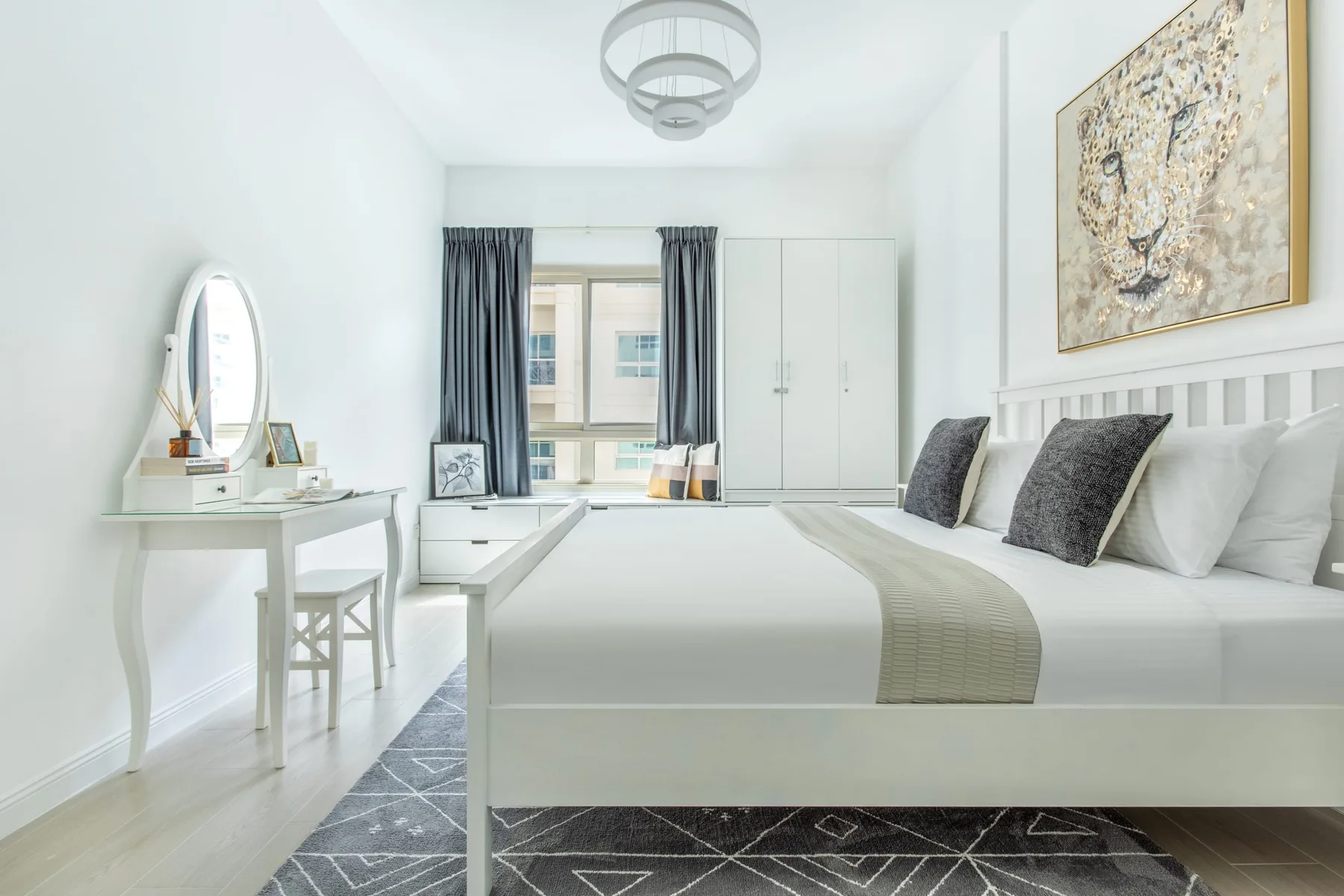Un dormitorio luminoso con una cama blanca, una ventana y un tocador.