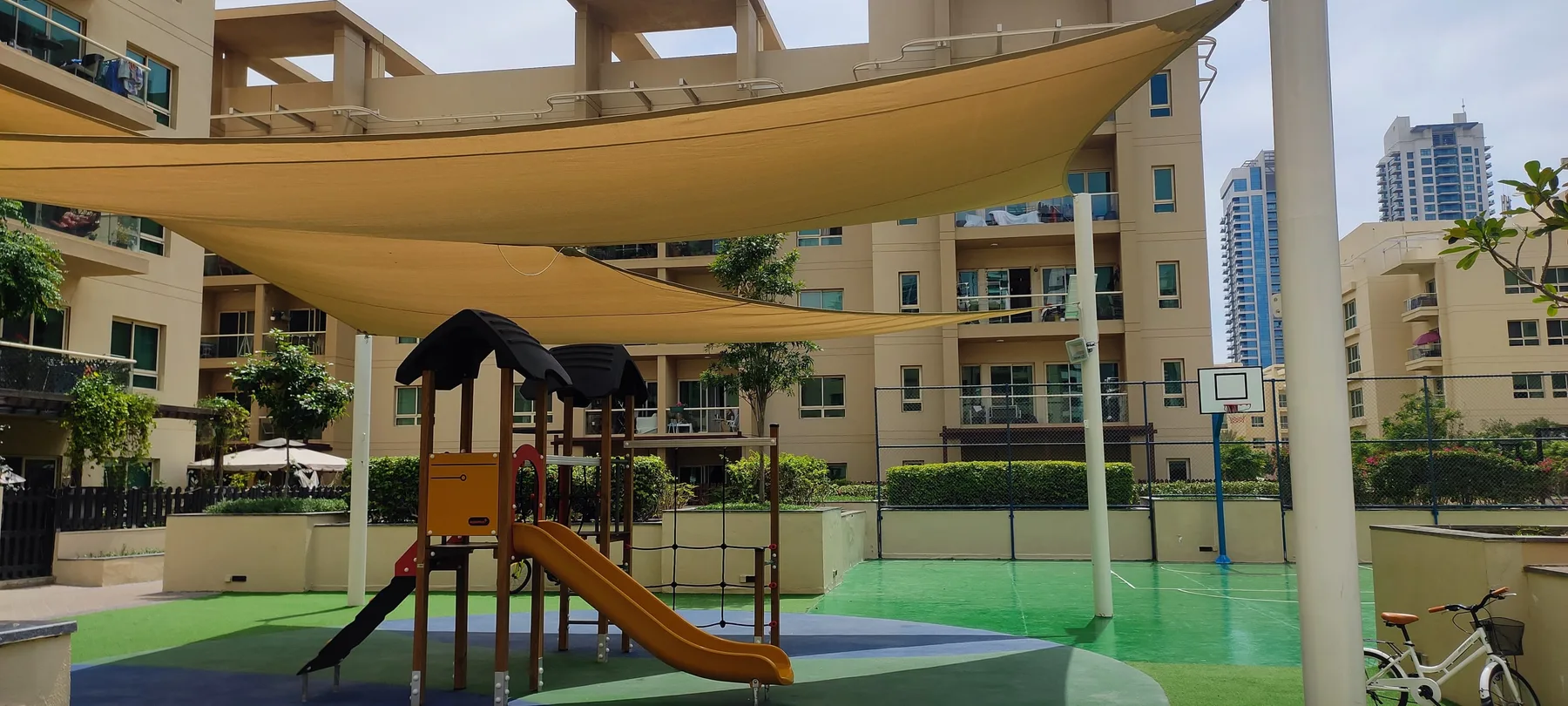 Un parque infantil al aire libre con una estructura para trepar está bajo una gran cubierta de sombra.