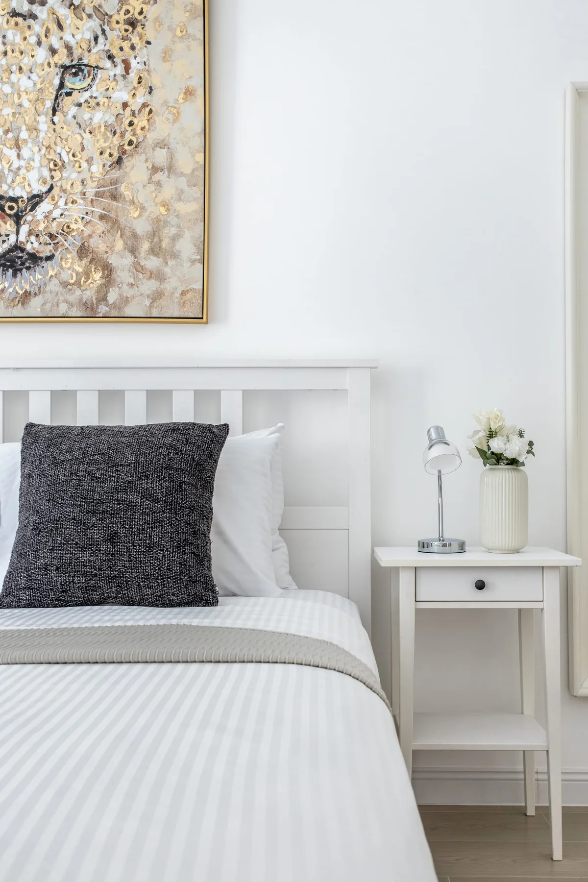 Un dormitorio luminoso con una cama bien hecha y un cuadro enmarcado sobre el cabecero.