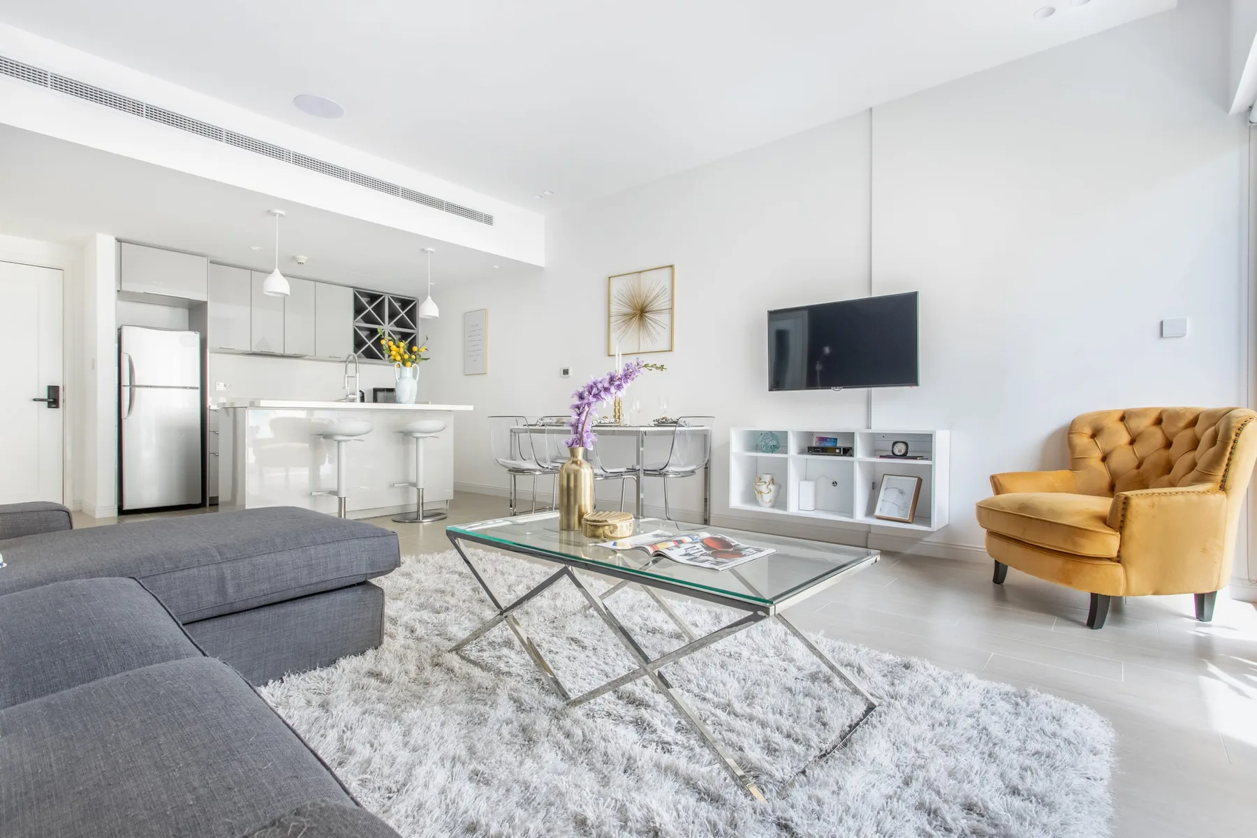 Una sala luminosa con una mesa de centro de vidrio y un televisor montado en la pared.
