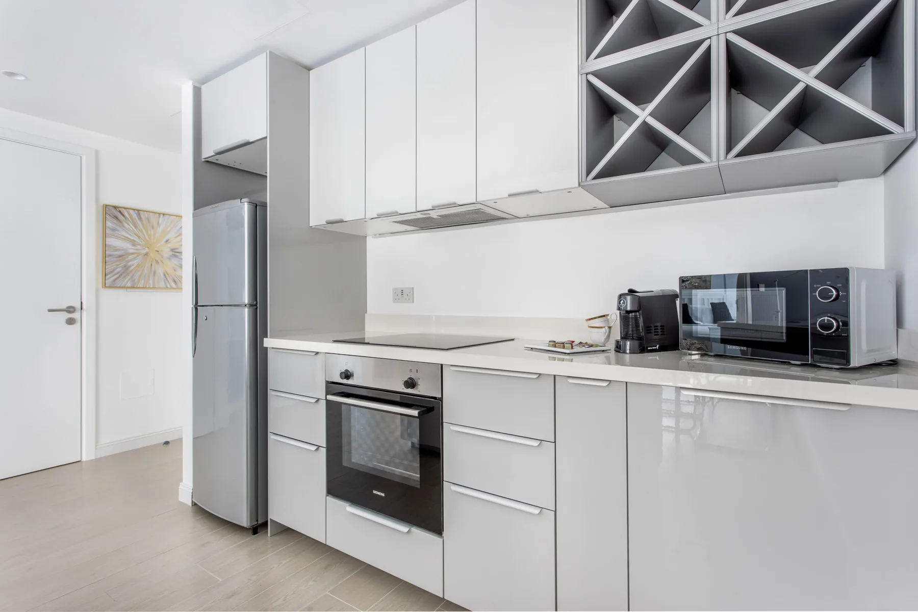 Una cocina moderna con armarios blancos, un refrigerador y electrodomésticos sobre la encimera.
