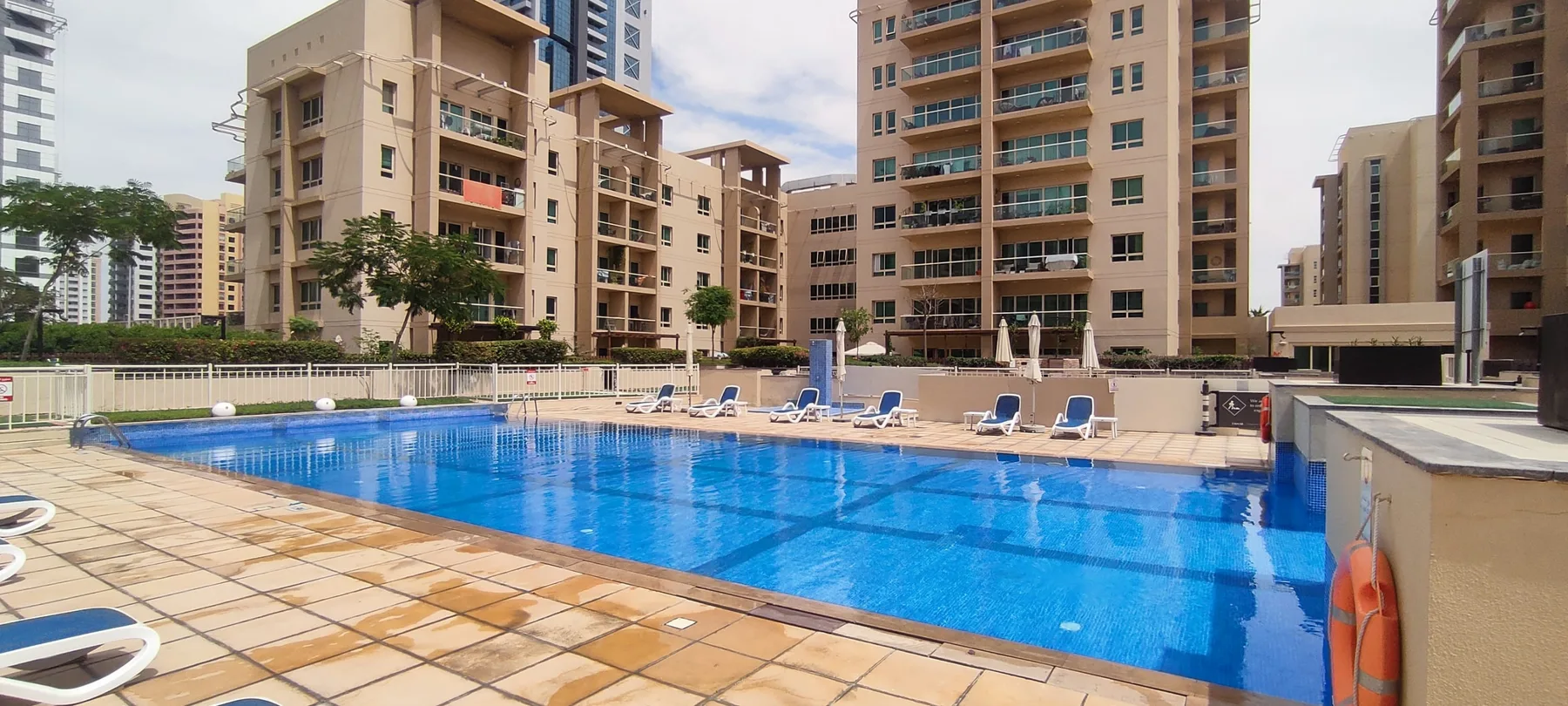 Una piscina al aire libre está rodeada de edificios de apartamentos y asientos en la terraza.
