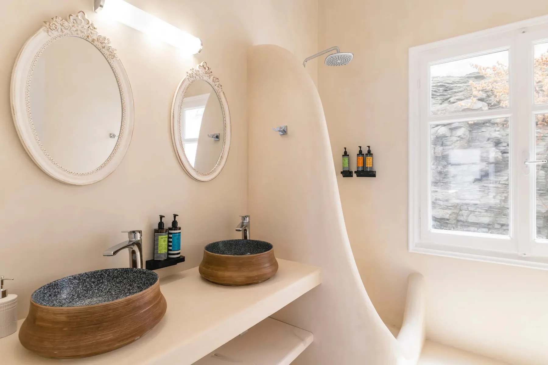 A bathroom vanity with two sinks and oval mirrors beside a shower.