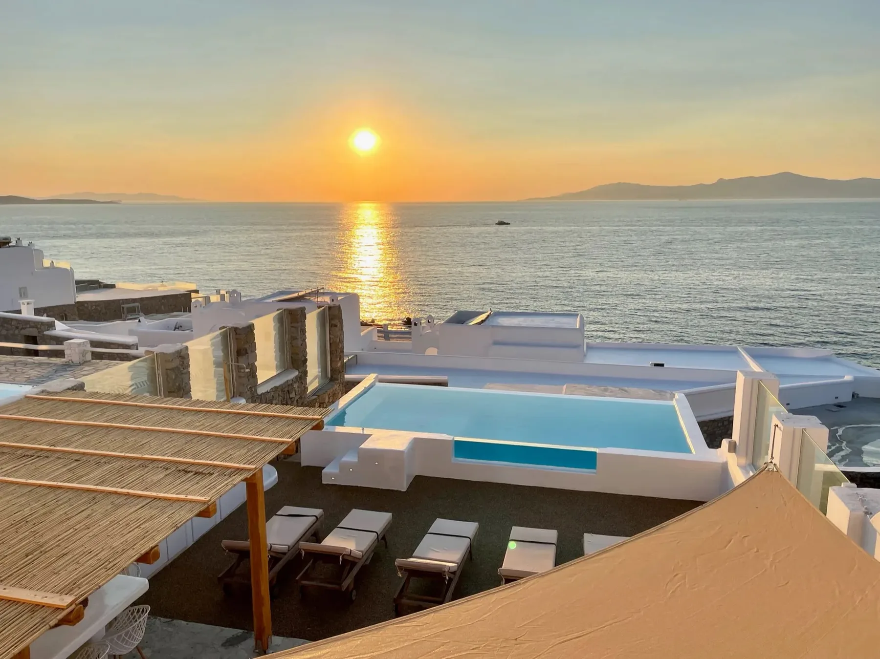 A seaside terrace with a swimming pool overlooks the water at sunset.