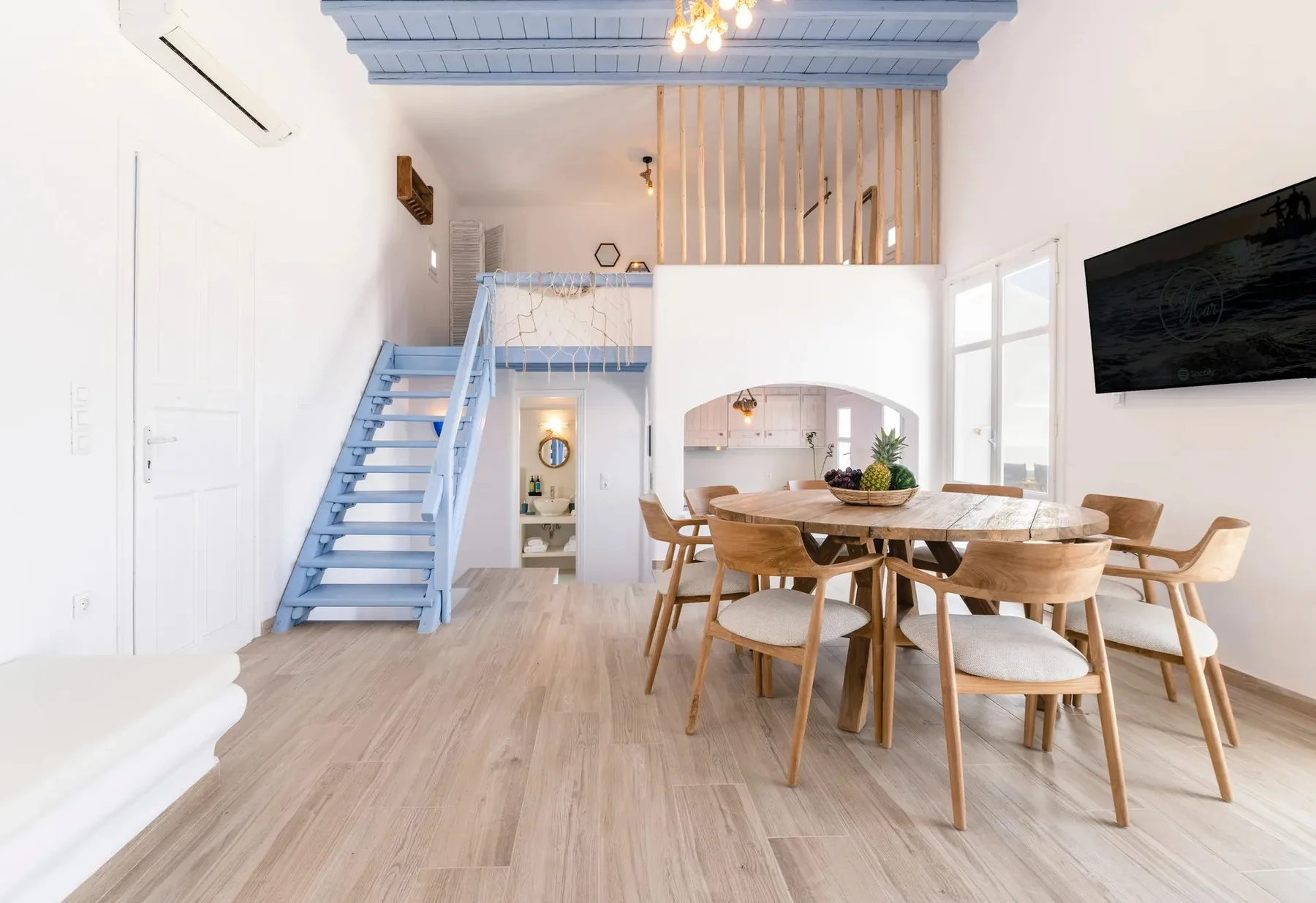 Un comedor luminoso con una mesa de madera, asientos y una escalera azul.