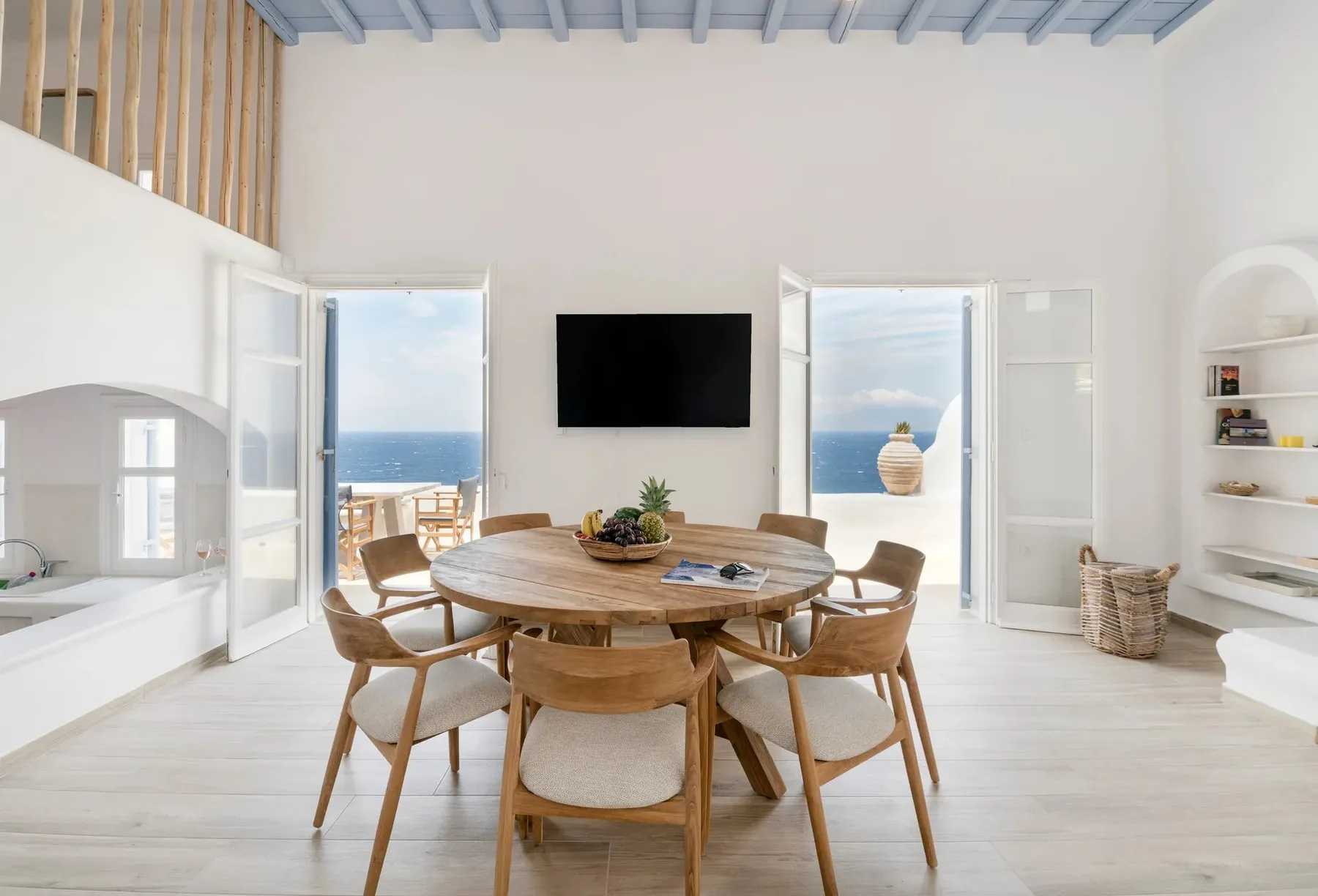 Un comedor luminoso con una mesa redonda de madera y vistas al mar por las puertas abiertas.