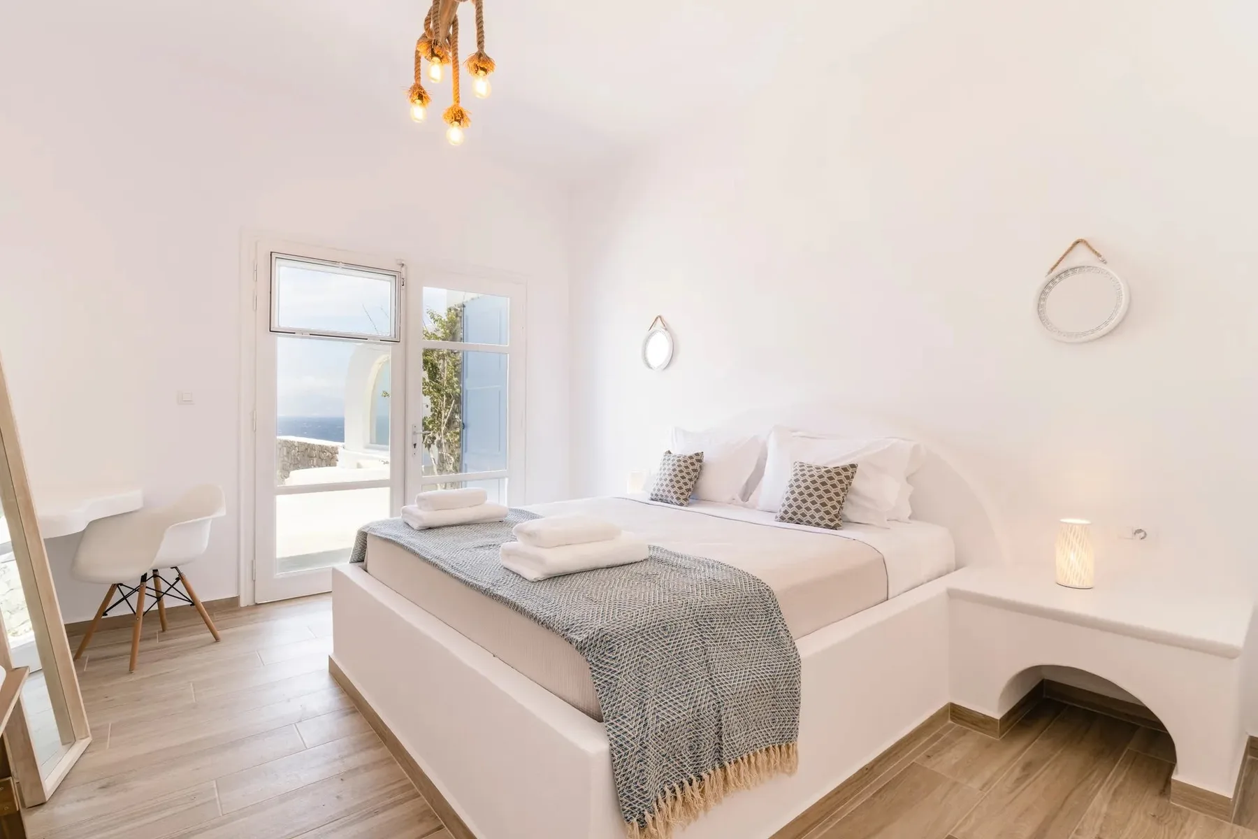 A bright bedroom with a neatly made bed and windows overlooking the water.