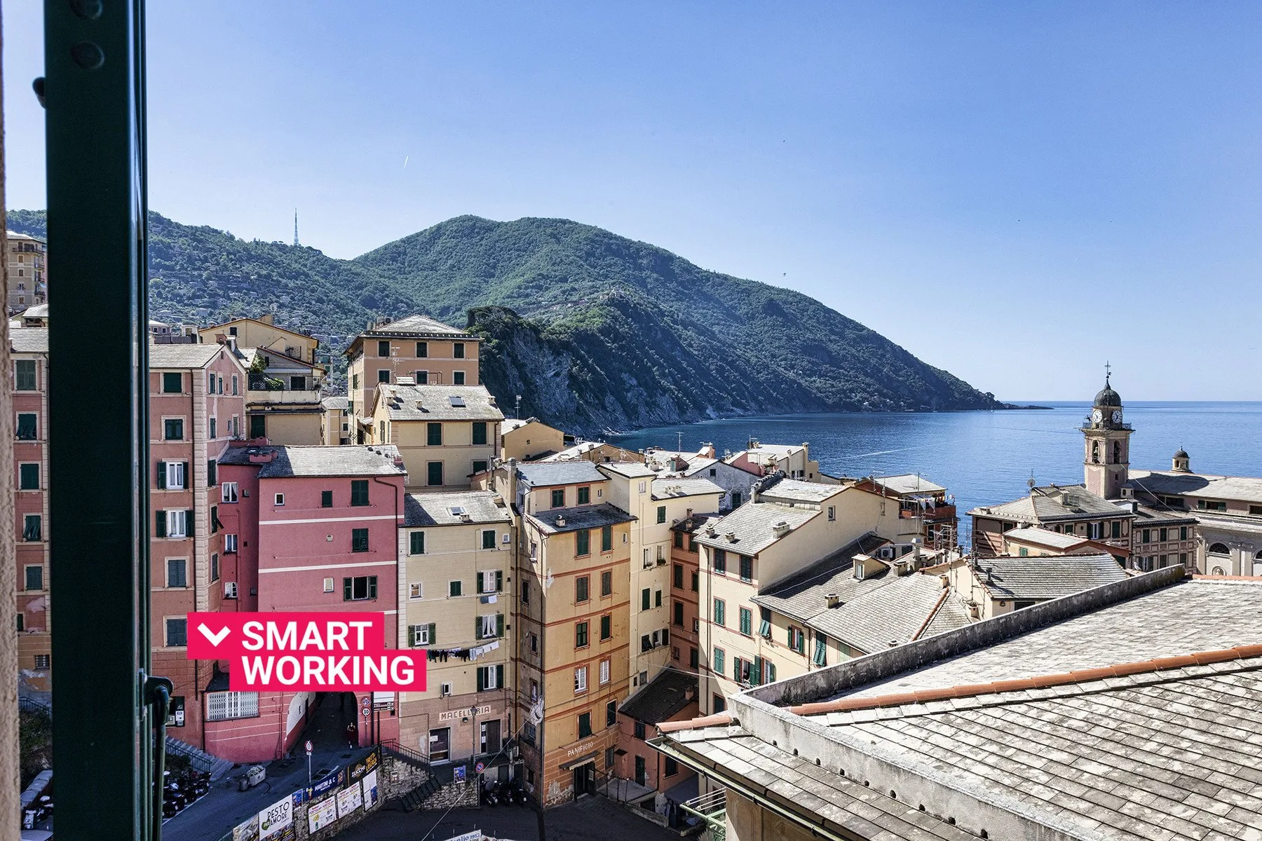 A coastal town’s colorful buildings overlook the bay and surrounding green hills.