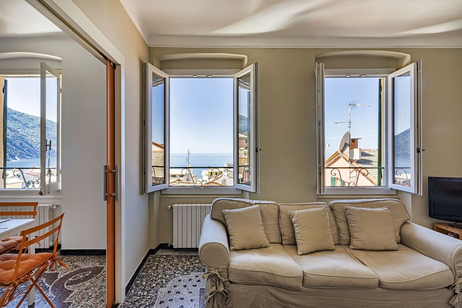 A living room with a beige sofa and open windows overlooking the sea.