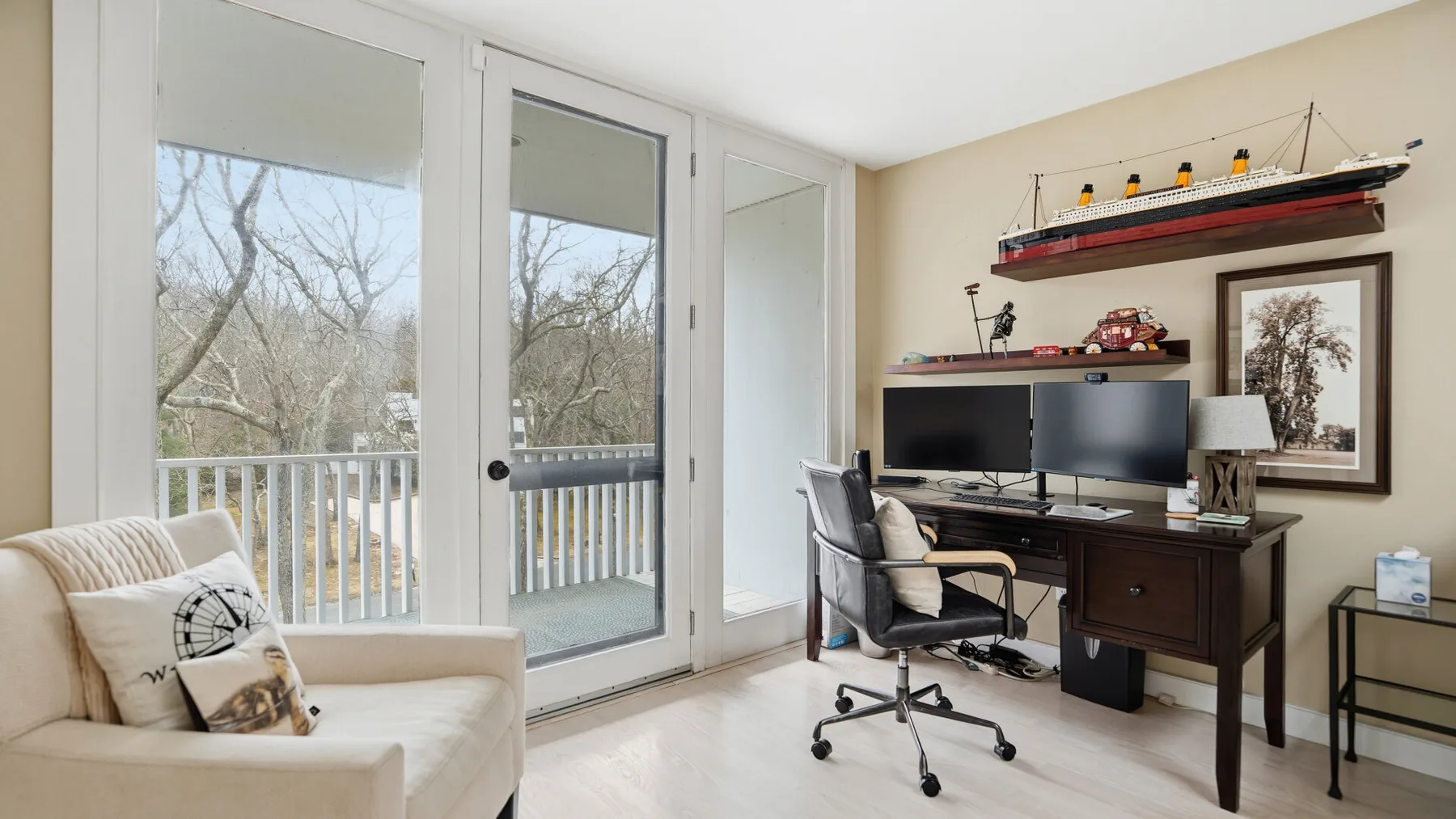 Una luminosa sala de estar y trabajo con un escritorio junto a ventanas altas y una puerta de cristal.