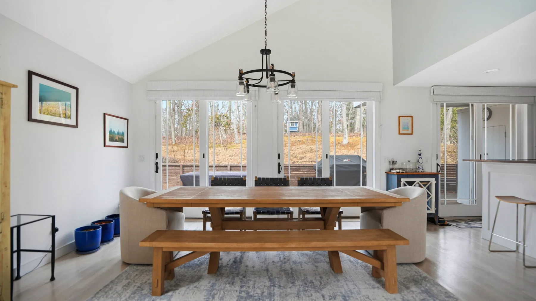 Un comedor luminoso con una larga mesa de madera y un banco junto a grandes ventanas.