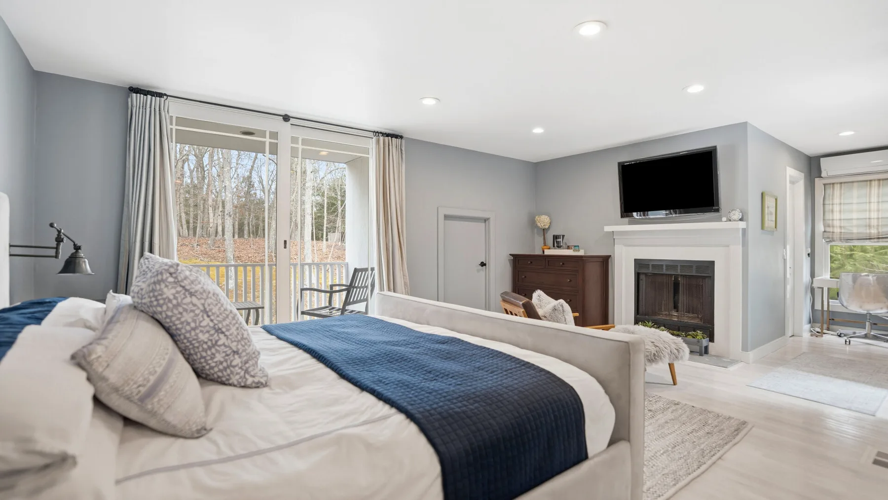 Un dormitorio luminoso con una cama frente a una chimenea y un televisor.