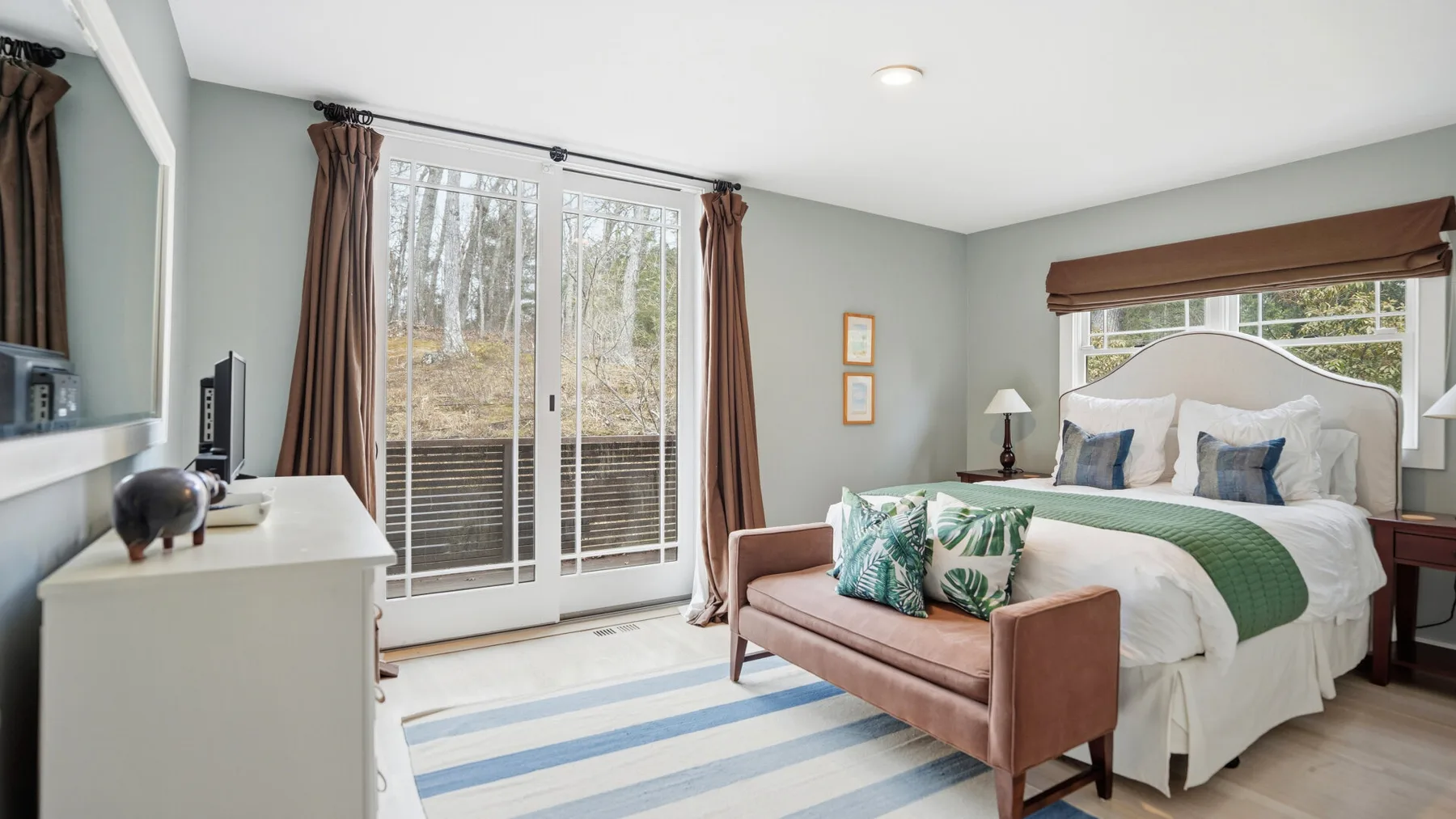 Un dormitorio con una cama, asientos tapizados y puertas de vidrio con vistas arboladas.