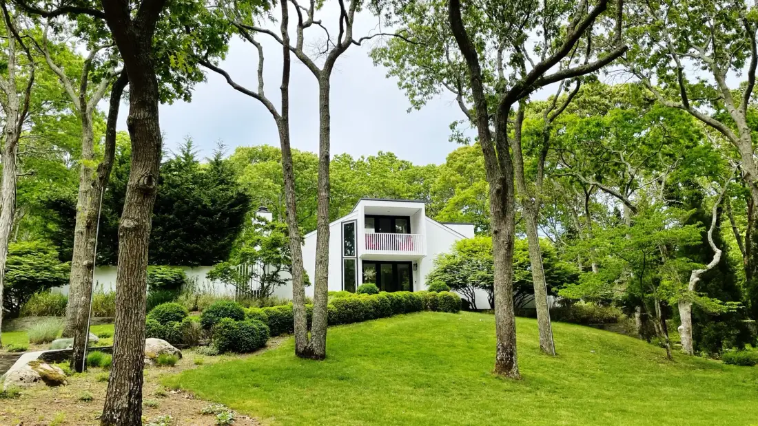 Una casa blanca moderna se encuentra entre árboles y jardines verdes.