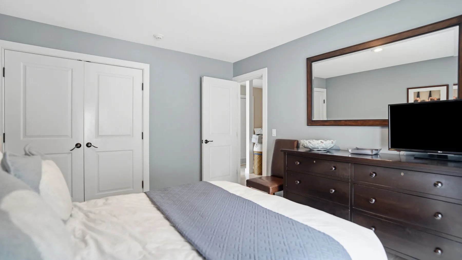 Un dormitorio con una cama, una cómoda oscura y un espejo grande en la pared.