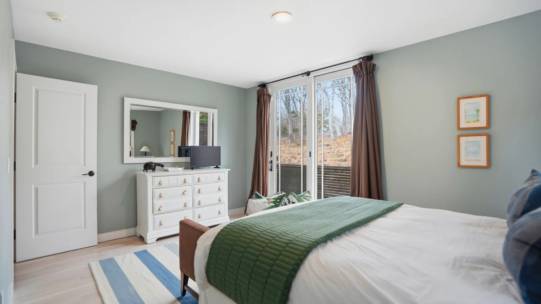 Un dormitorio con una cama bien tendida y grandes ventanas con vista a los árboles.