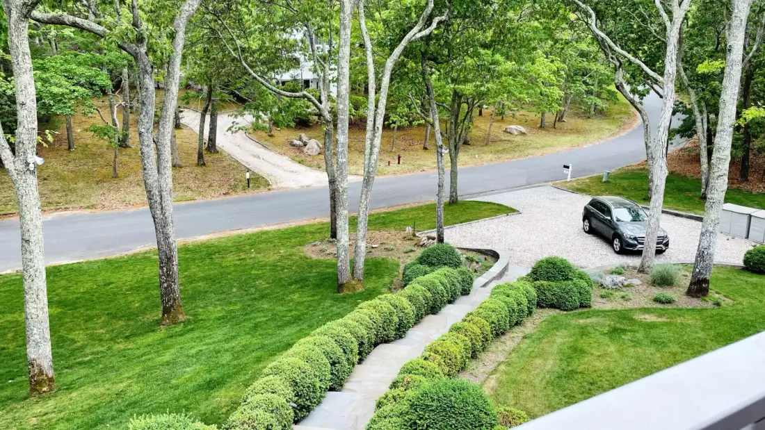 Un jardín cuidado con un sendero curvo, setos recortados y un automóvil estacionado.