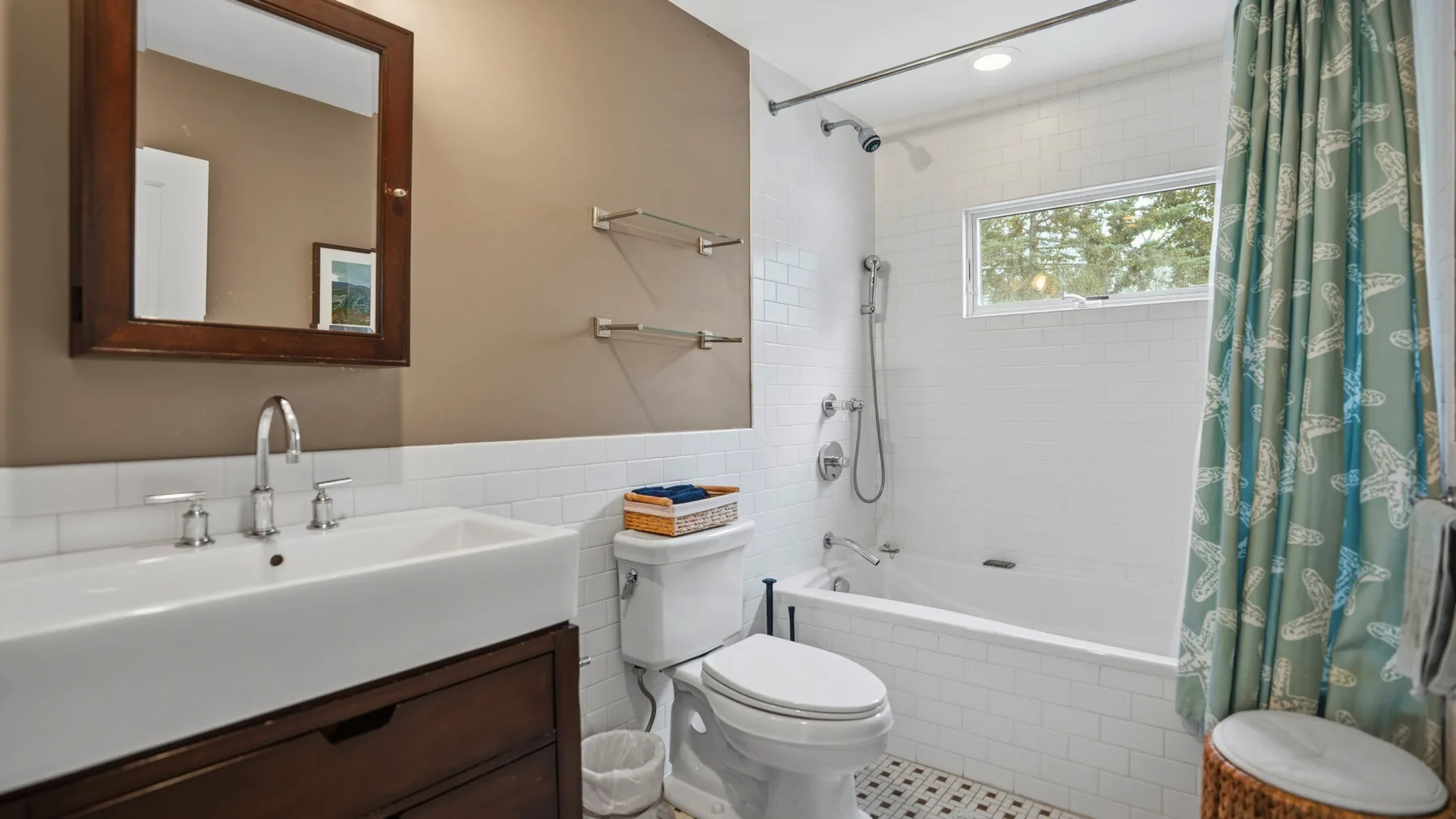 Un baño con lavabo, inodoro y bañera detrás de una cortina de ducha estampada.