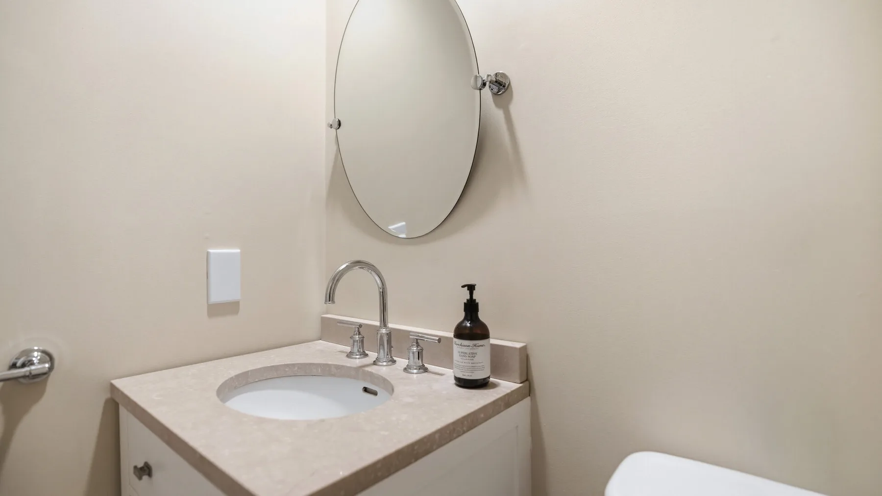 Un tocador de baño con lavabo, grifo, espejo ovalado e inodoro.