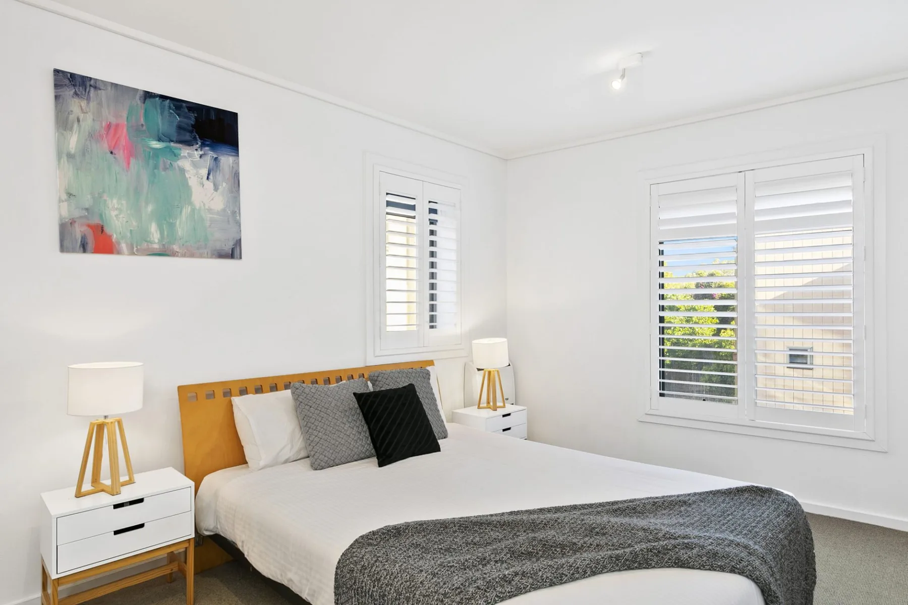 Un dormitorio luminoso con una cama tendida y arte abstracto en la pared.