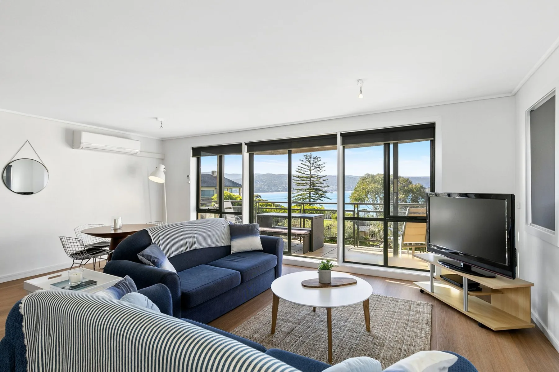 Sala de estar con asientos, un televisor y grandes ventanas con vista al agua.