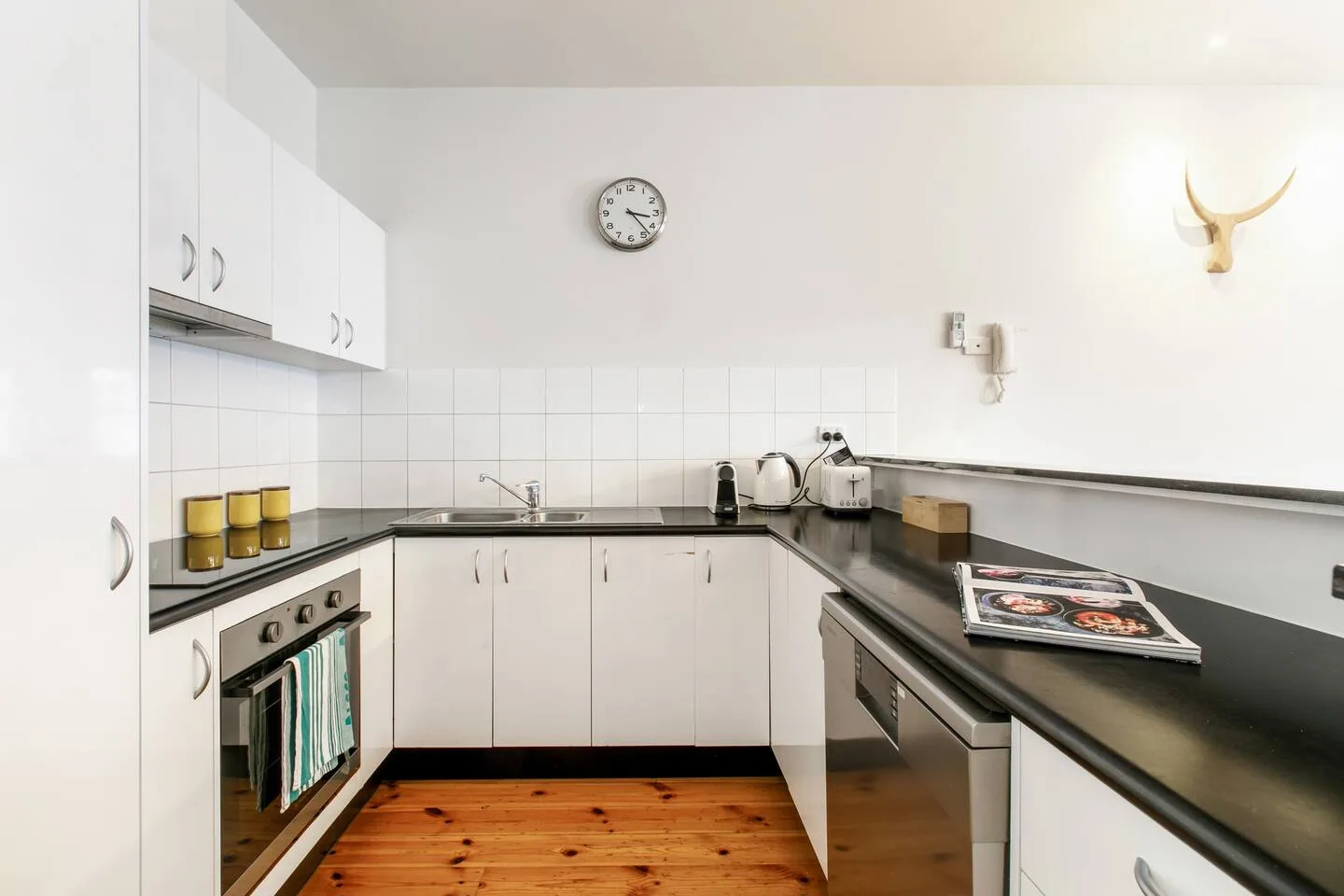 Una cocina con gabinetes blancos, encimeras oscuras y suelo de madera.