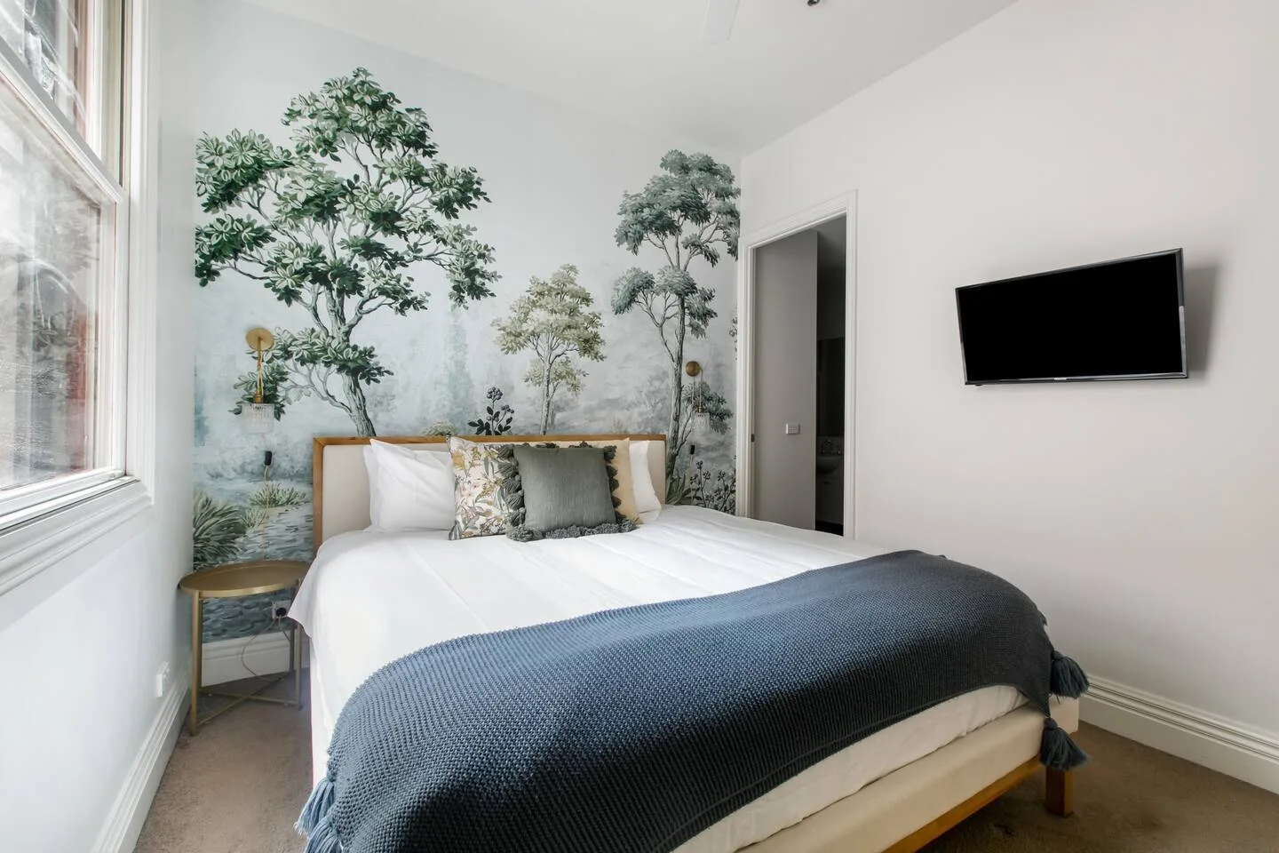 A bedroom with a neatly made bed and a wall-mounted television.