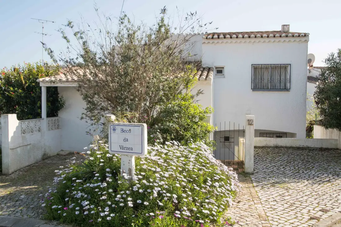 Una casa blanca junto a un camino de adoquines y un jardín con flores.