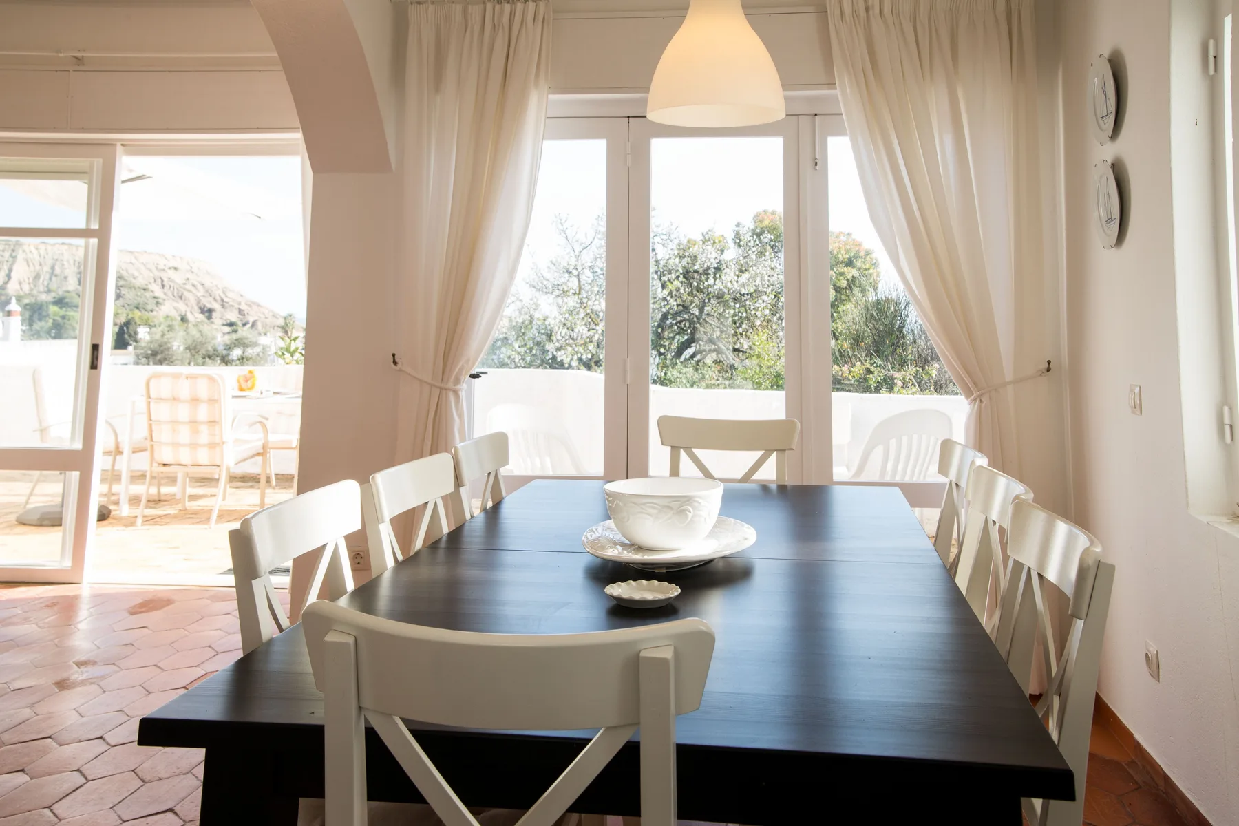 Comedor con una mesa larga y sillas blancas junto a ventanas luminosas.