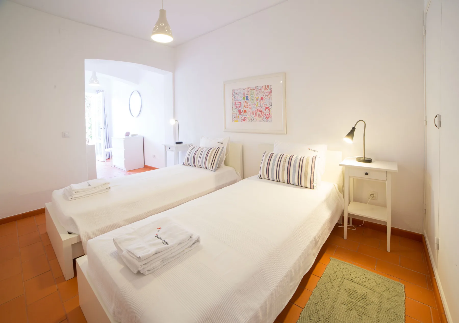Un dormitorio luminoso con camas, una mesilla y un cuadro enmarcado.