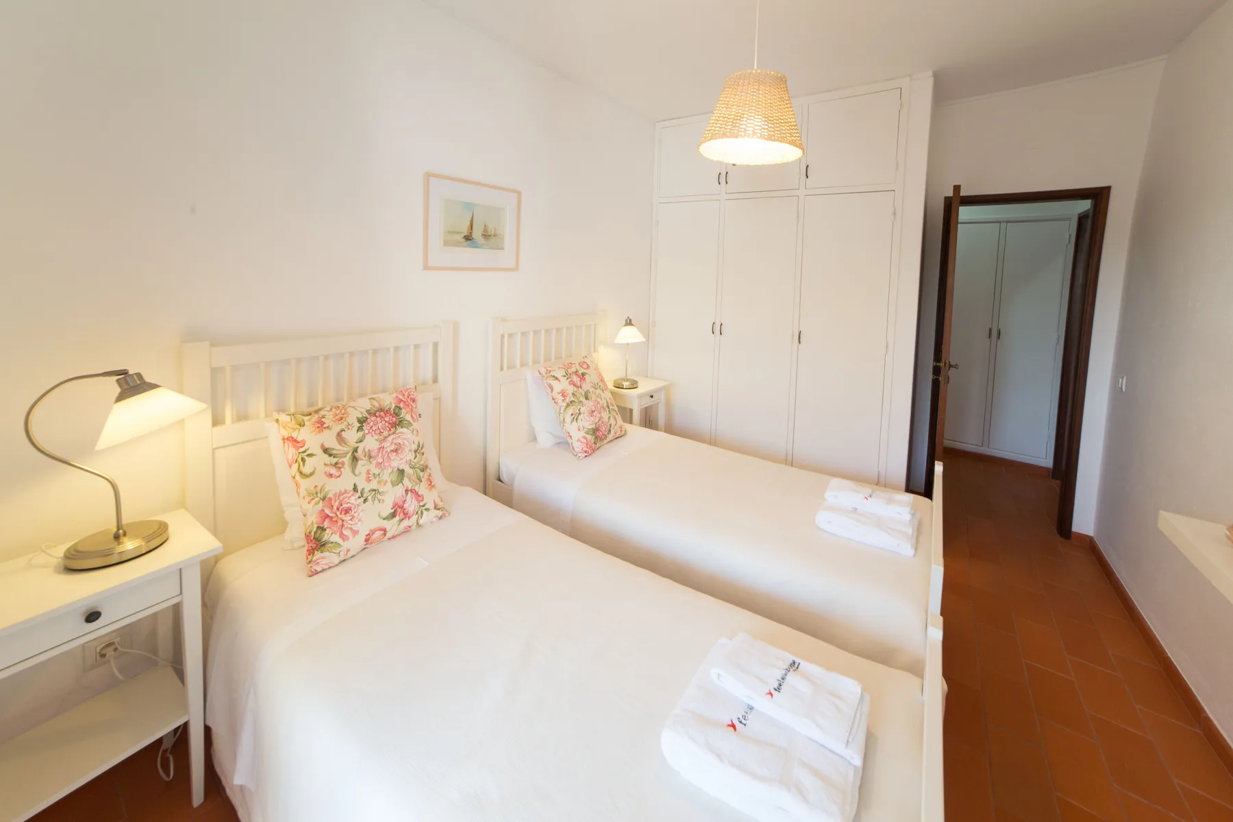 Un dormitorio luminoso con dos camas, cojines florales y un armario.