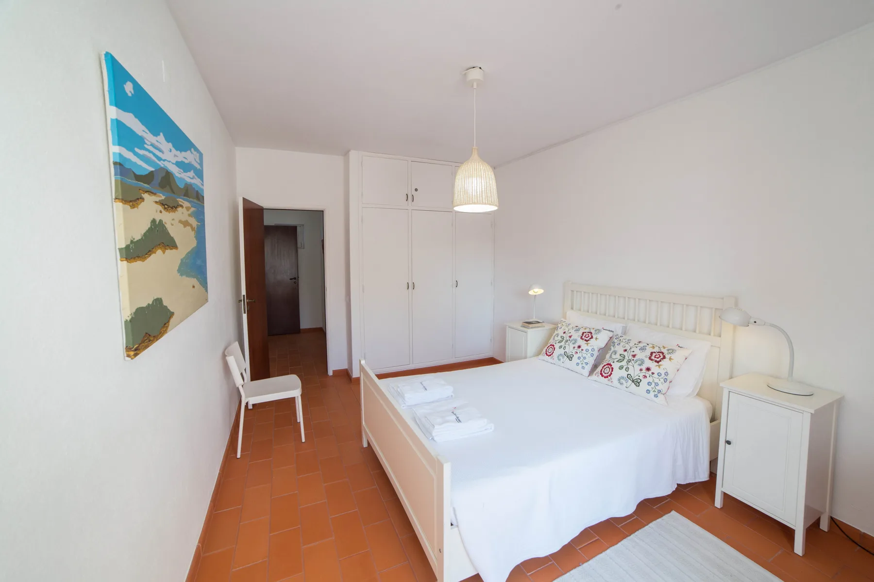 Un dormitorio luminoso con una cama blanca, mesillas y suelo de baldosas.