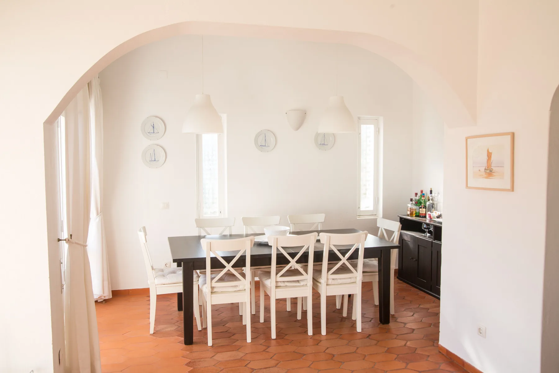 Un comedor con una mesa larga y sillas blancas bajo un arco.