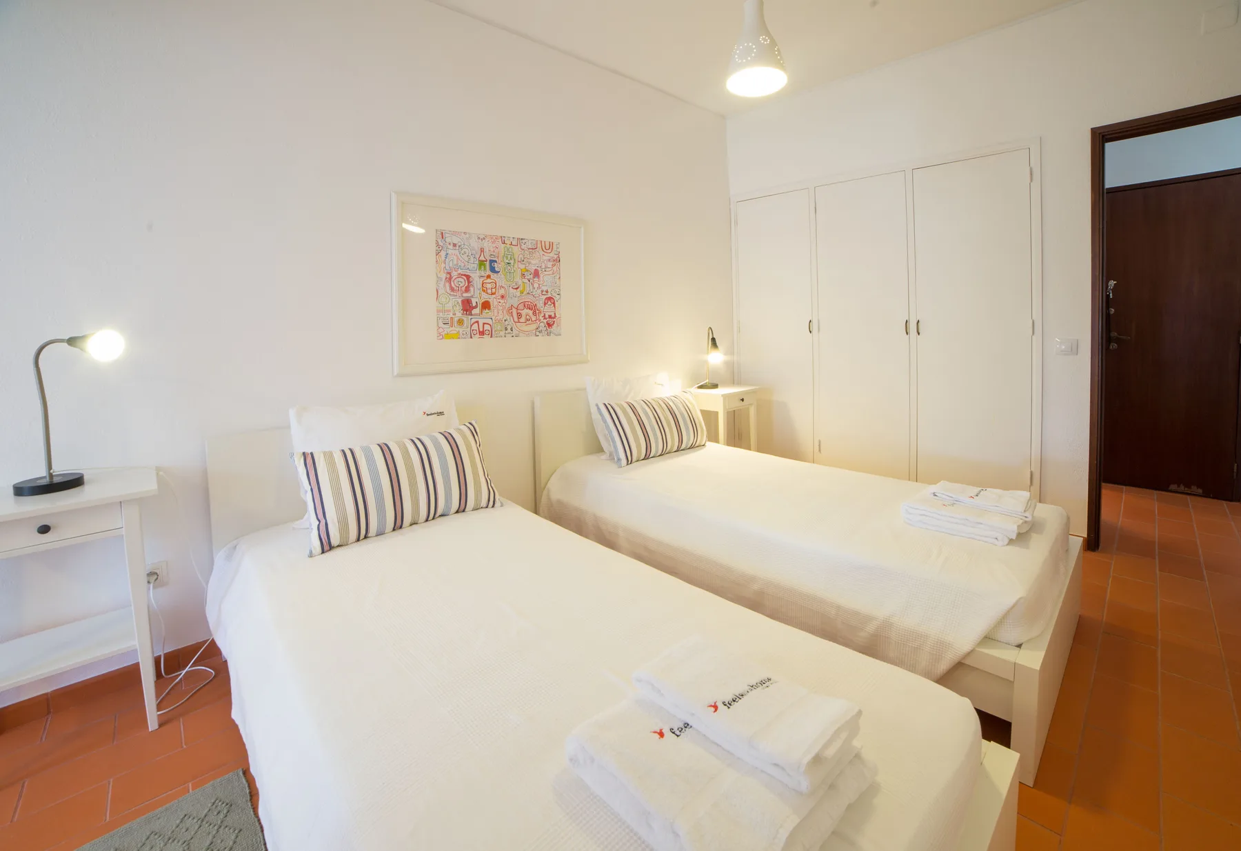 Un dormitorio luminoso con dos camas, mesitas de noche y un cuadro enmarcado.