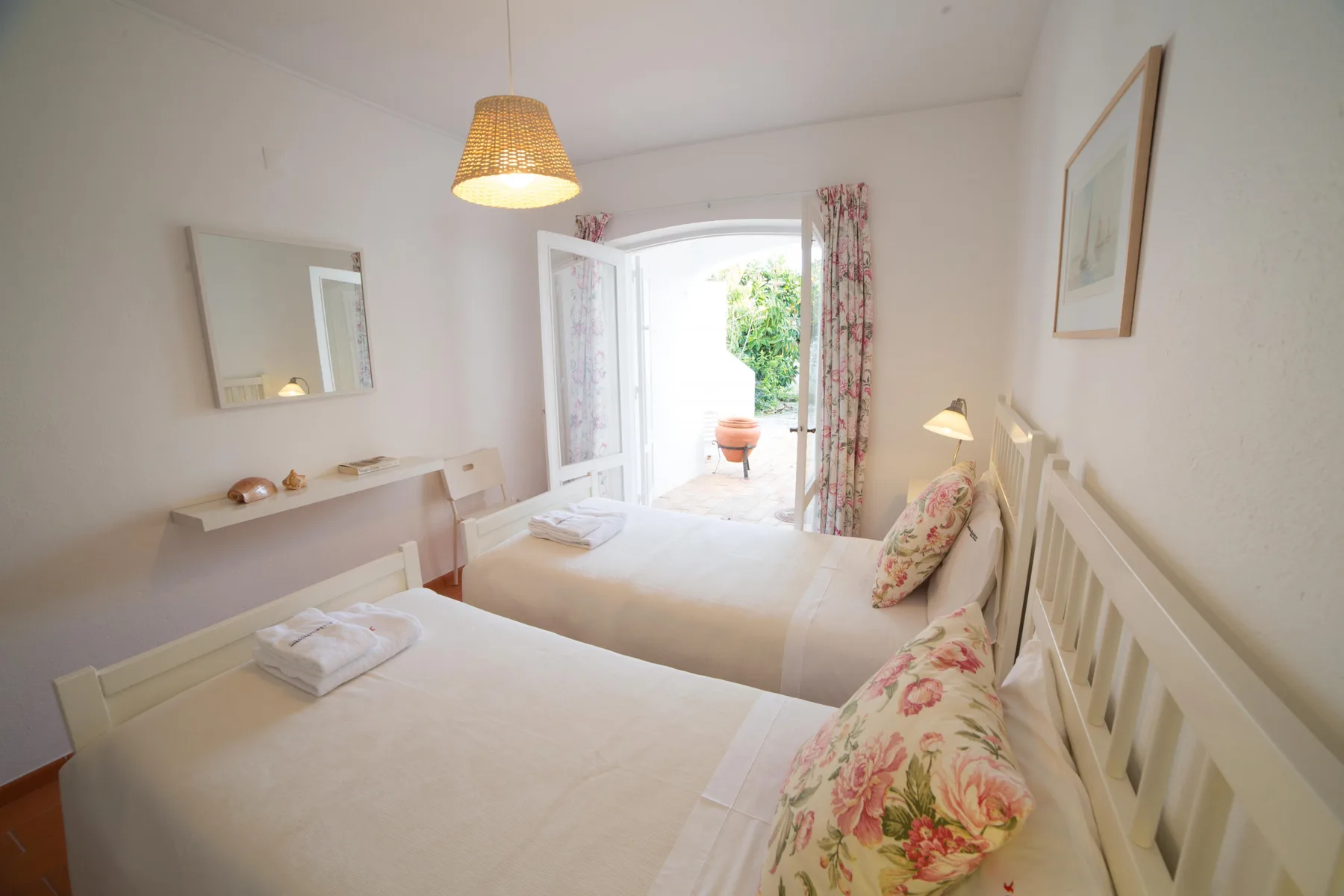 Un dormitorio luminoso con dos camas y una puerta abierta que da a un patio.