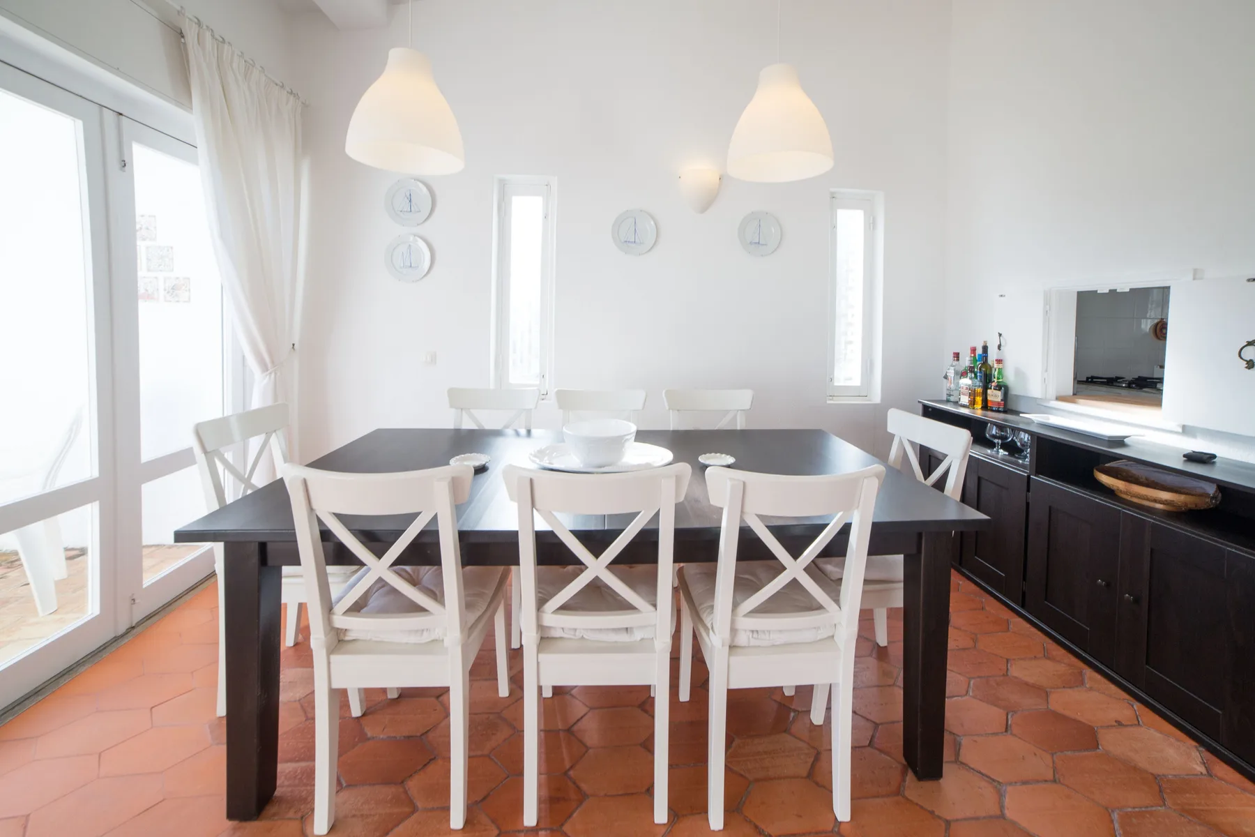 Comedor con una mesa oscura y sillas blancas junto a una ventana grande.