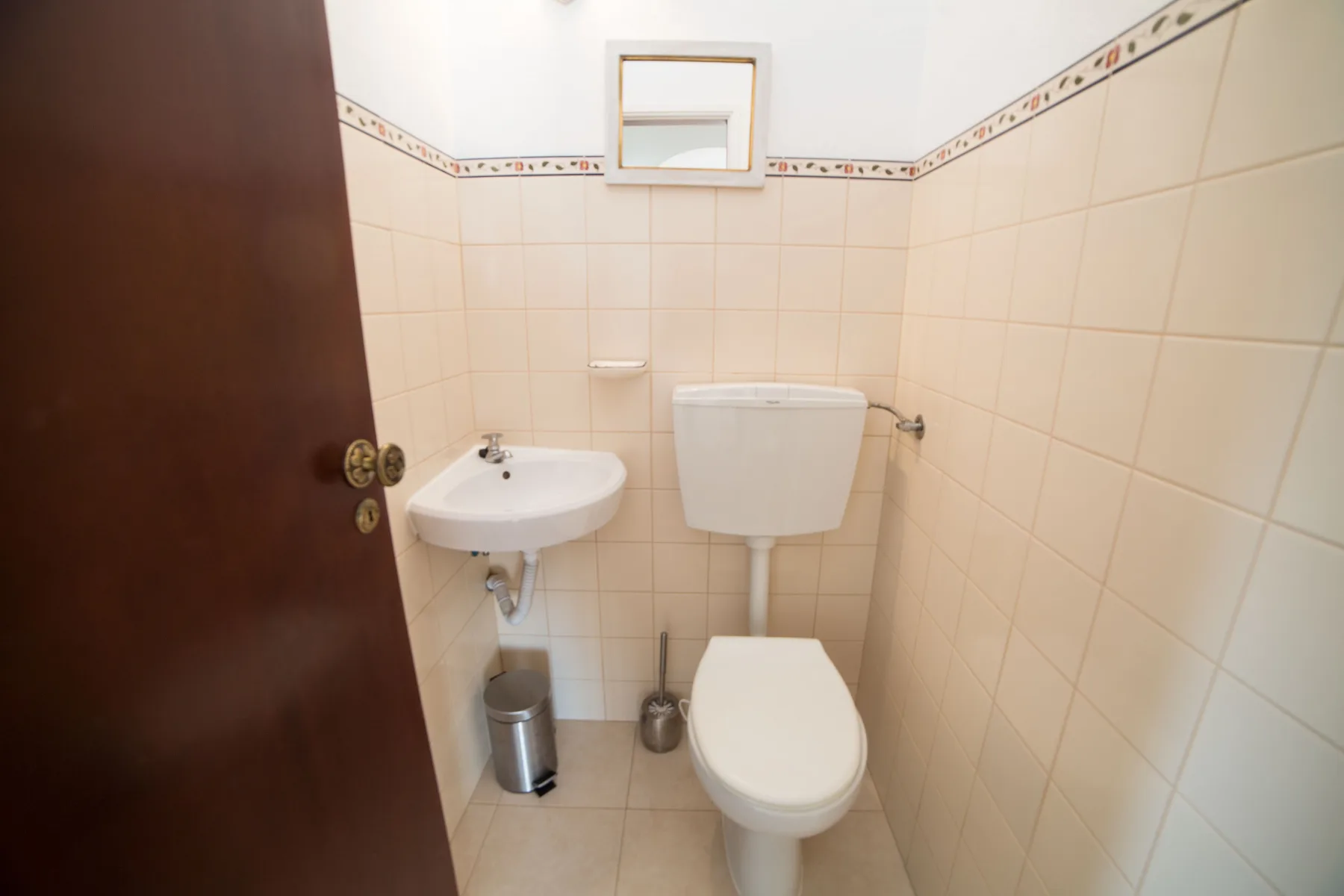 Un baño alicatado con un inodoro y un pequeño lavabo de pared.