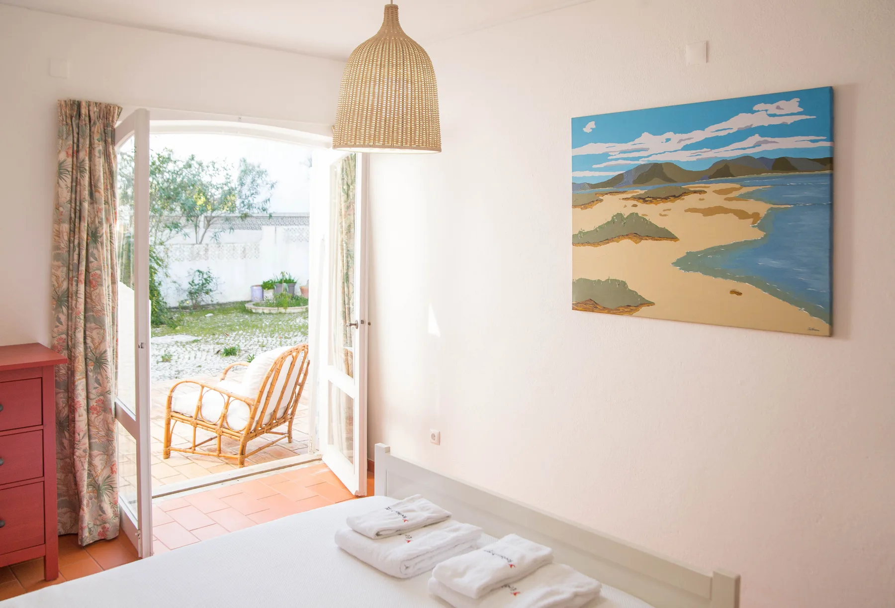 Dormitorio con toallas dobladas junto a una puerta abierta que da a un patio.
