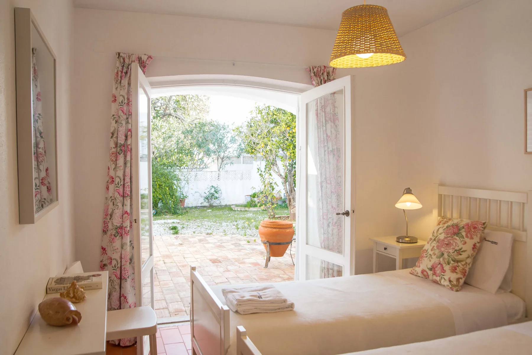 Un dormitorio se abre a un patio embaldosado con vegetación a través de puertas de cristal.