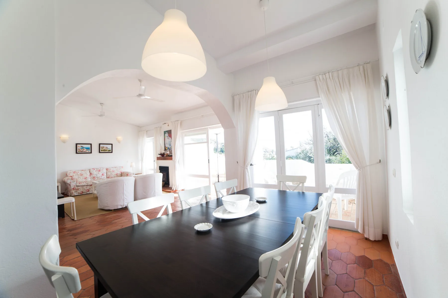 Un comedor luminoso con una mesa oscura junto a grandes ventanas con cortinas.