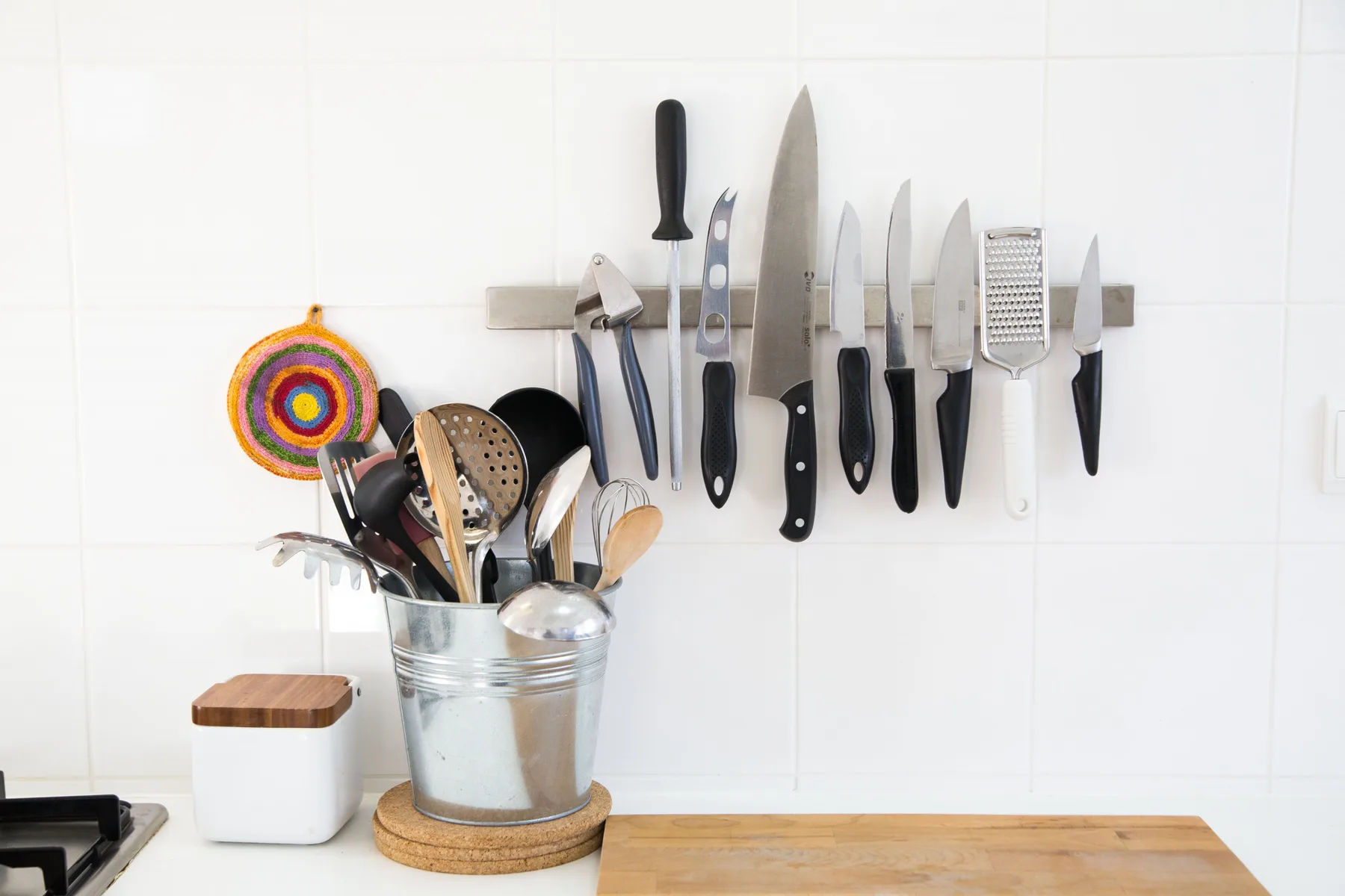 Utensilios de cocina y cuchillos están colocados en una pared alicatada sobre una encimera.